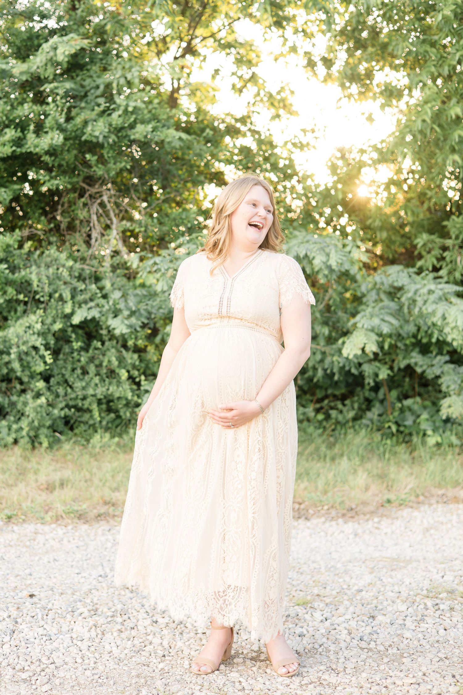 mom in cream colored lace dress laughs during maternity session in mckinney texas with mckinney maternity photographer at erwin park