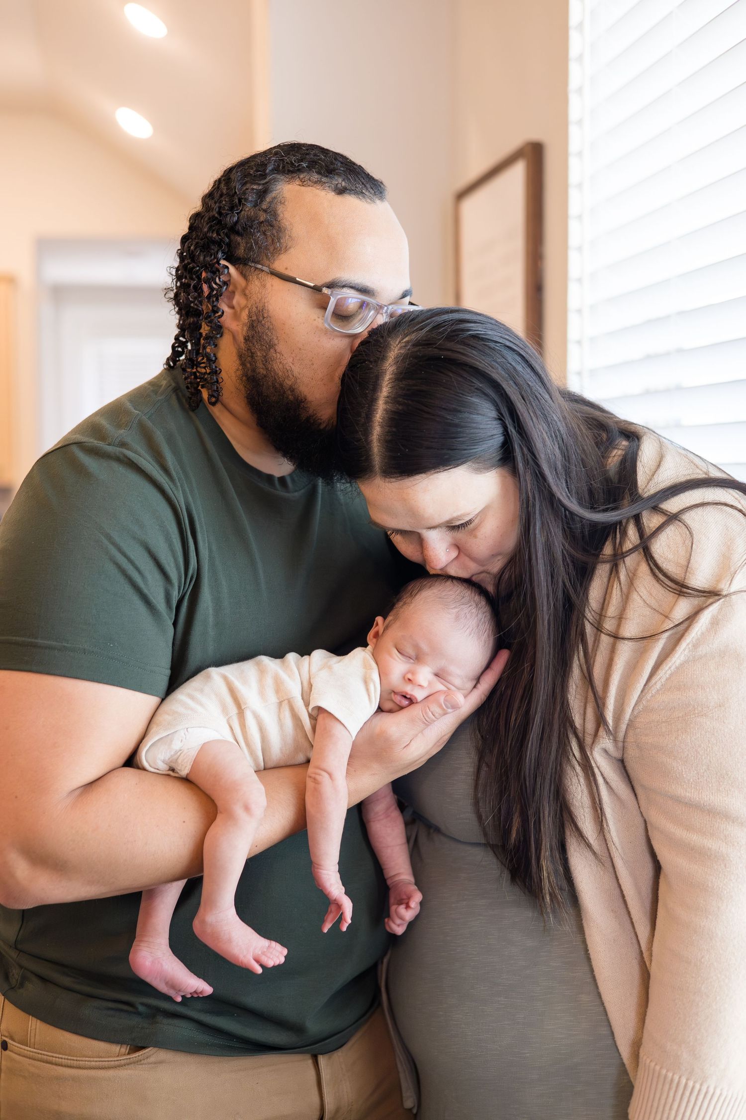 dad kisses mom while mom kisses baby during lifestyle newborn session with Reagan Marie Photography, McKinney based photographer