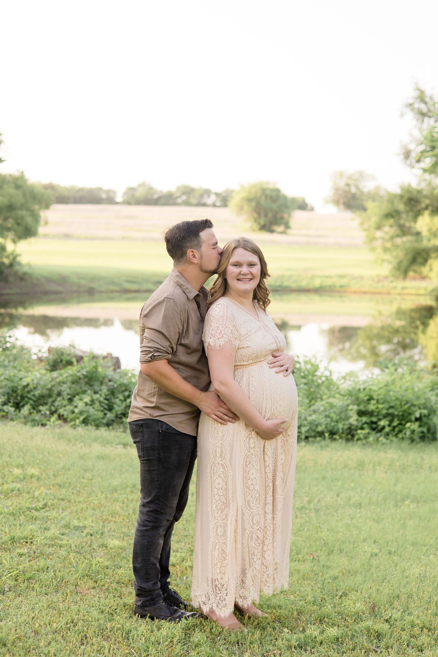 dad kisses mom during maternity portraits at erwin park in front of pond with maternity photographer based in mckinney texas