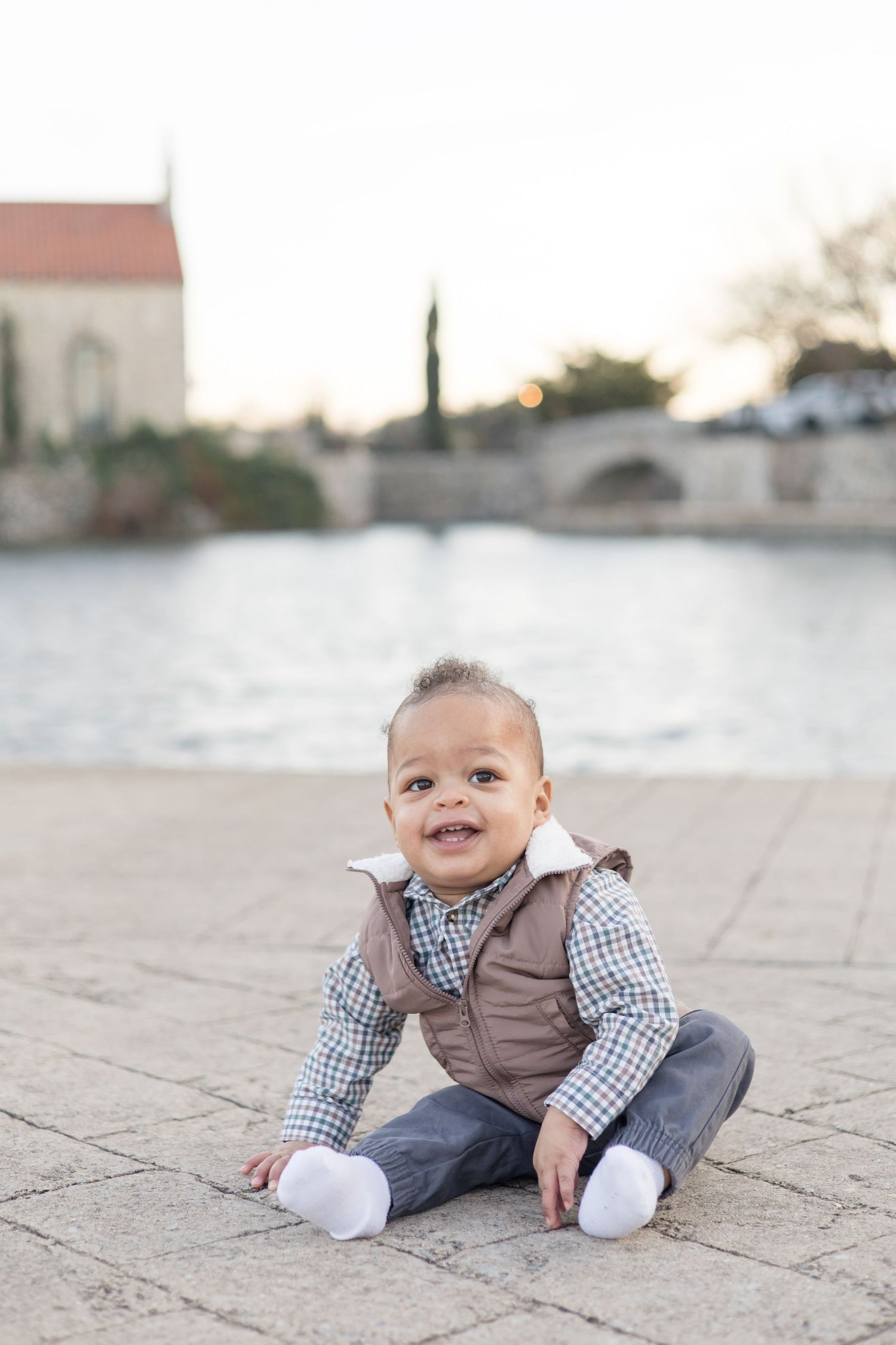Toddler boy sits on sidewalk during family portrait session with Reagan Marie Photography in McKinney, TX at Adriatica Village.