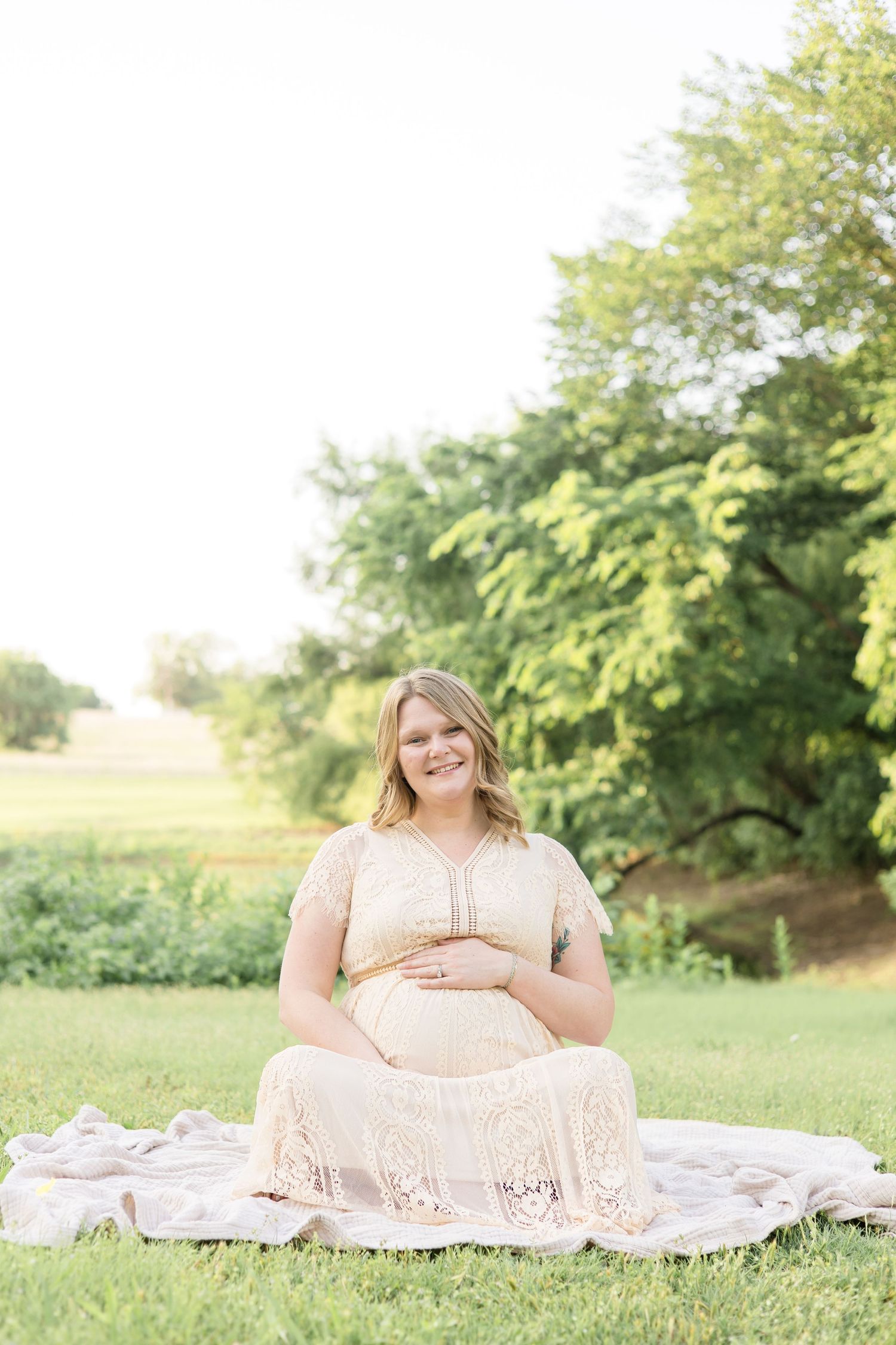 expecting mother sits on blanket in front of pond at erwin park during maternity session with mckinney based photographer