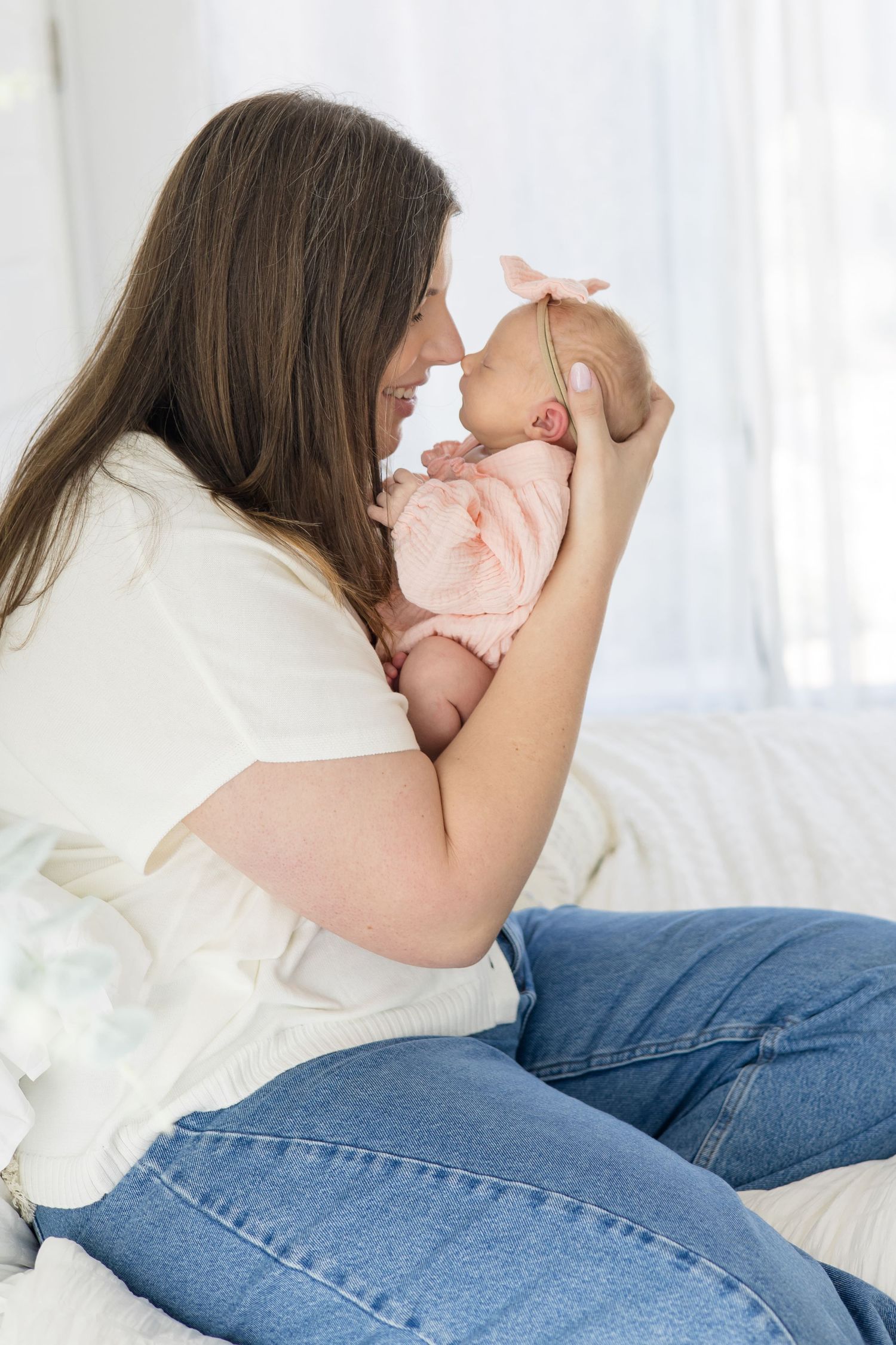 Mom in white button up and jeans holds daughter in pink outfit and bow up to touch noses during family lifestyle session at McKinney studio