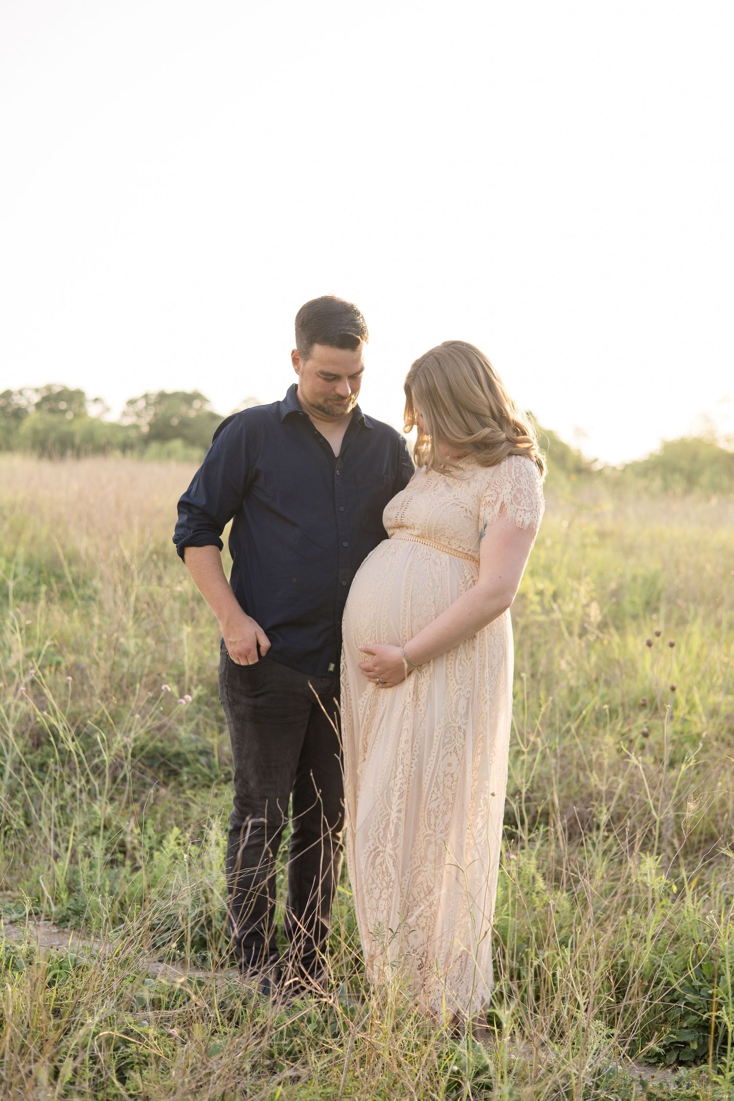 mom and dad look lovingly at mom's pregnant belly during maternity portrait session with dallas family photographer