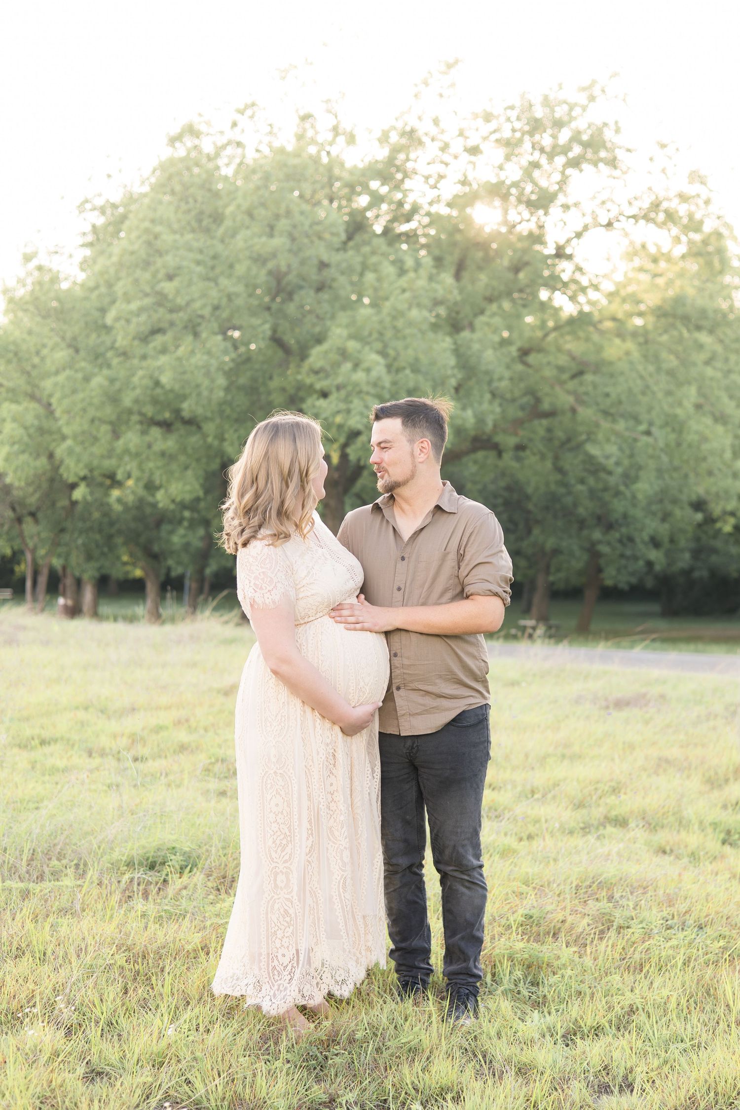 expecting mom and dad look at one another lovingly during maternity portrait session with mckinney family photographer at erwin park