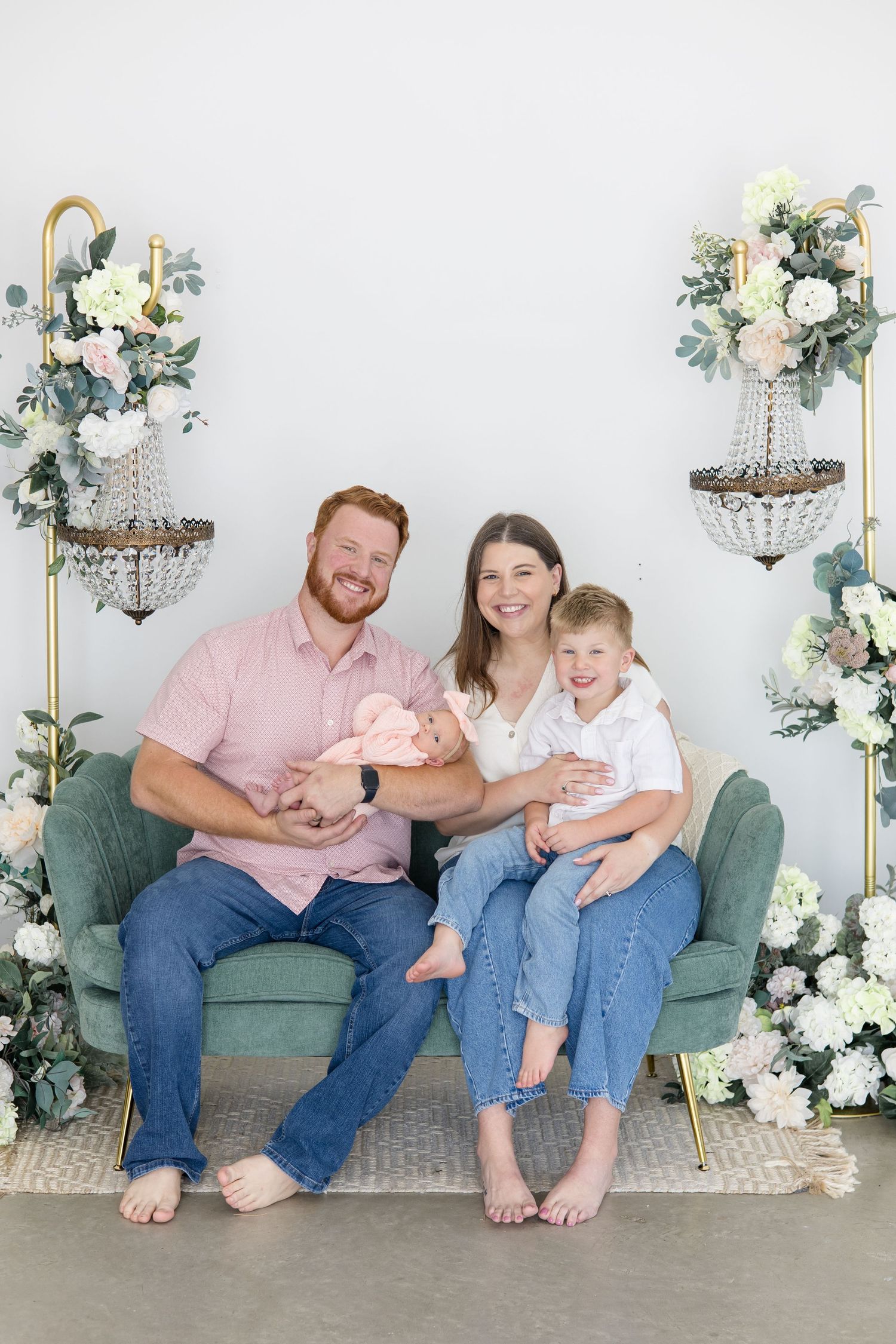 Family of 4 sits on green couch together during lifestyle newborn session in the summer at Lemon Drop Studio with Reagan Marie Photography