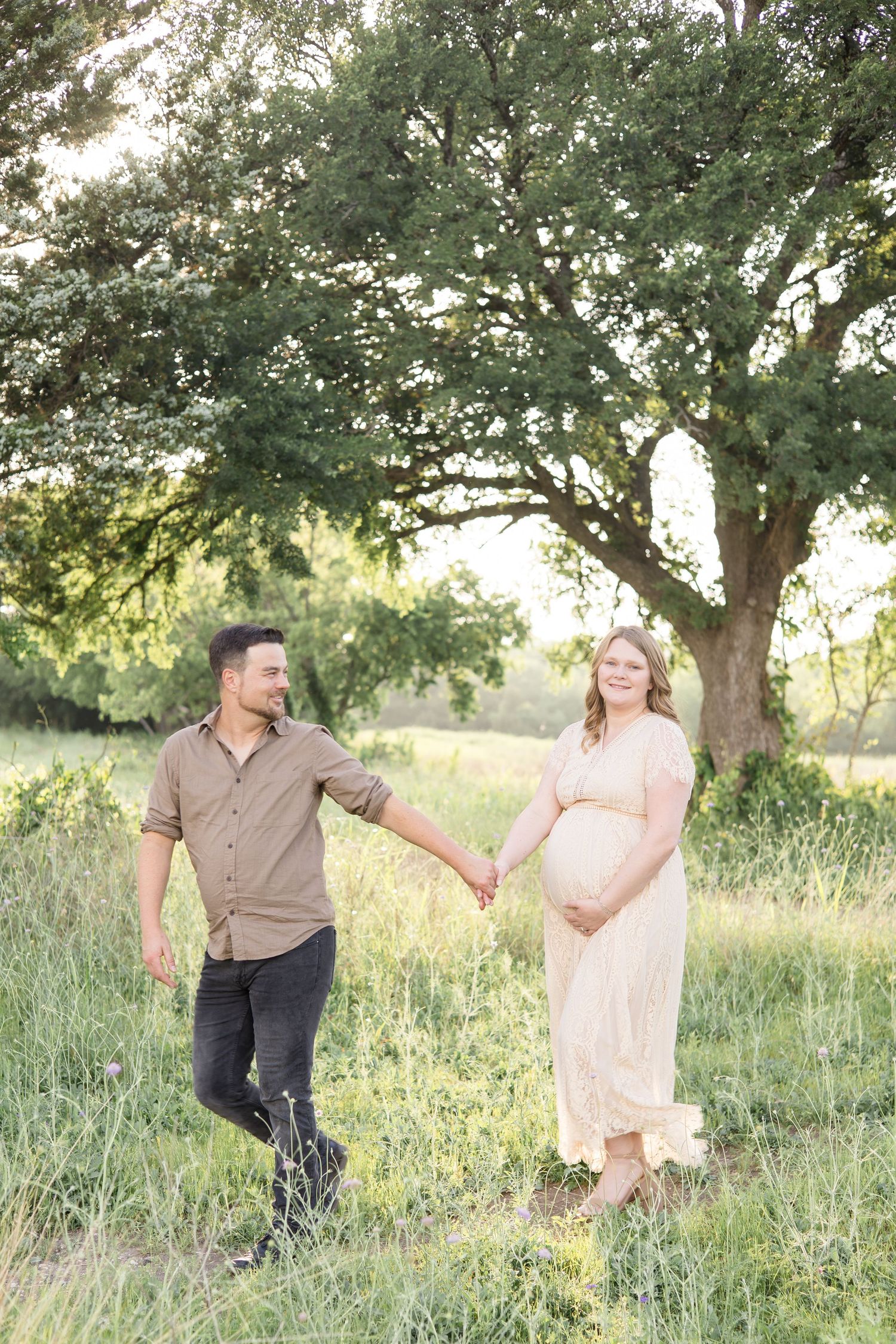 mom and dad walk hand in hand during maternity portrait session in the spring at erwin park in mckinney texas