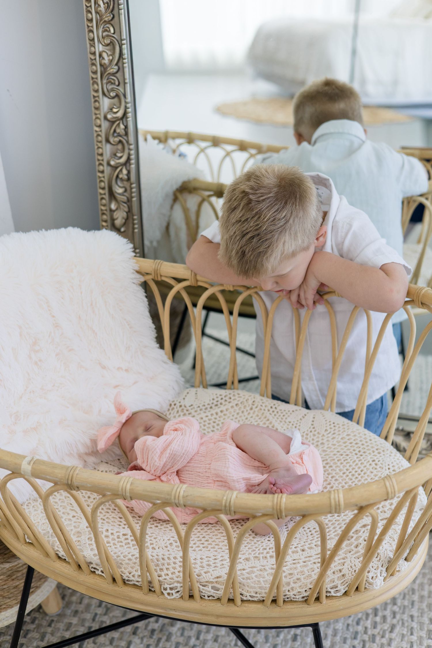 Older brother watches baby sister in wicker bassinet during lifestyle newborn session in studio with McKinney newborn photographer