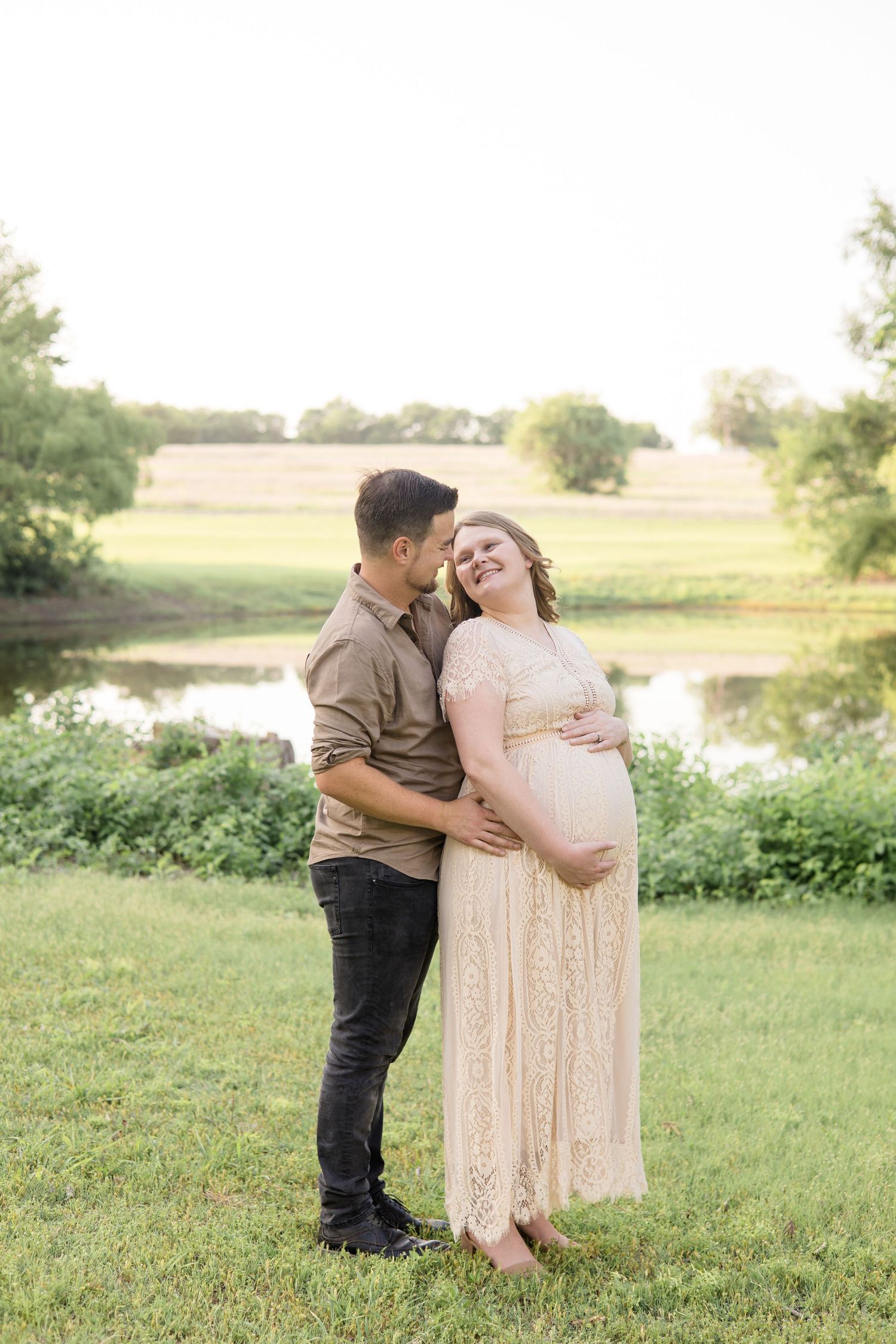 Expecting parents pose in front of pond at erwin park in mckinney texas during golden hour maternity session with dallas family photographer