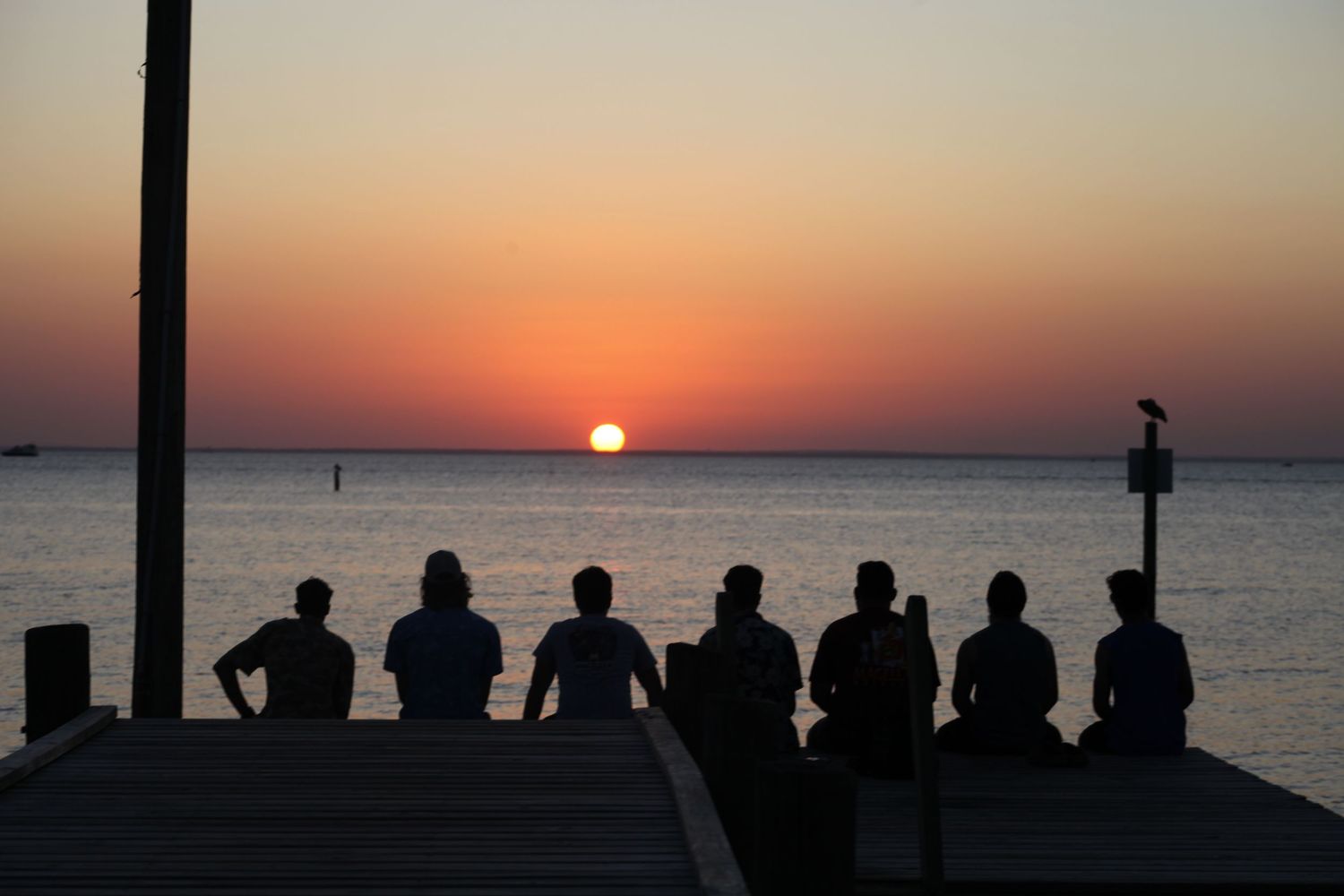 A group of men sitting on a dock looking into the sunset