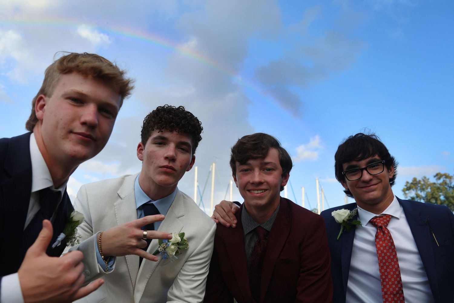 Four men posing in suits in front of a rainbow