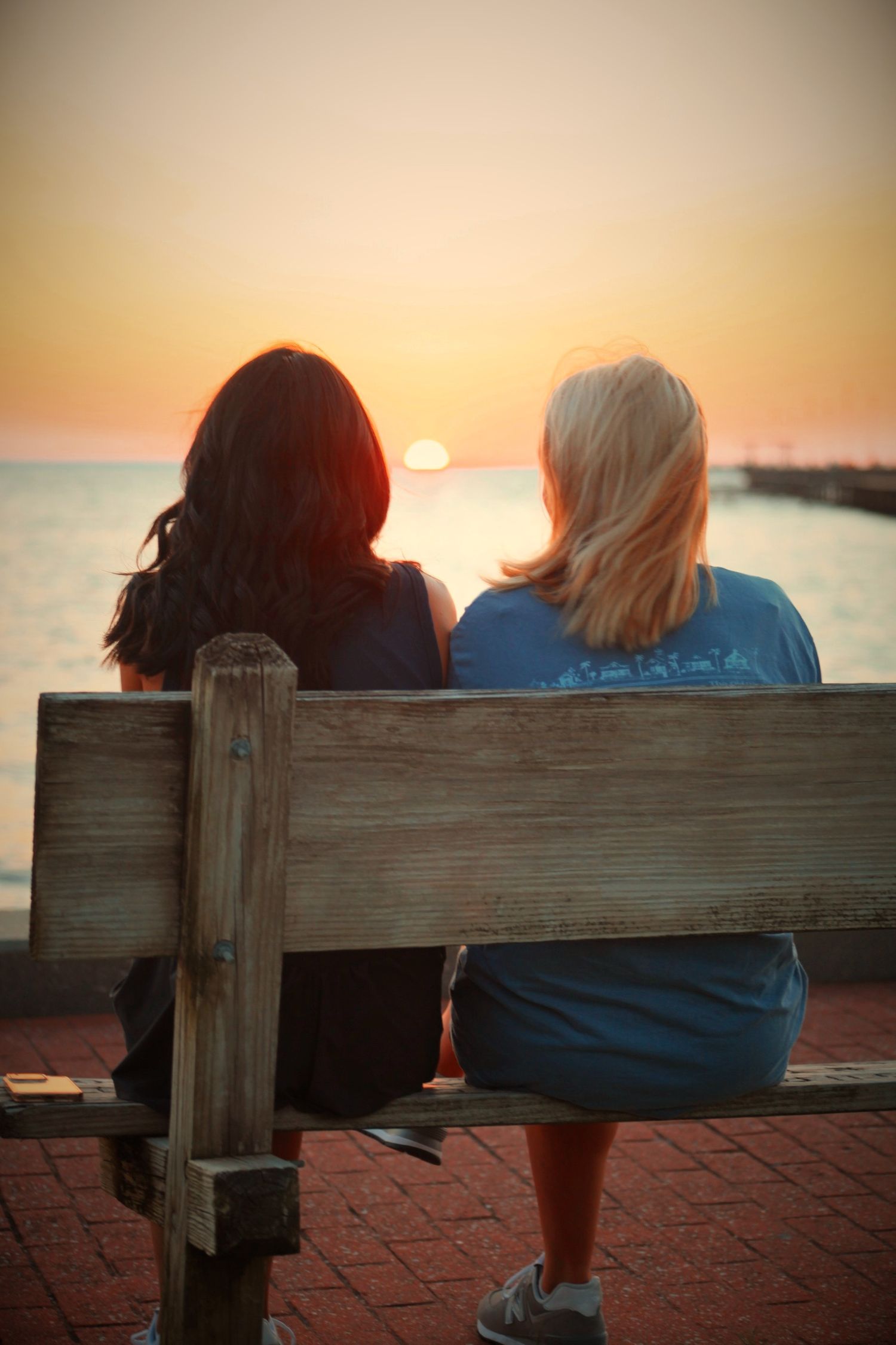 Two girls sitting on a bench watching the sunset