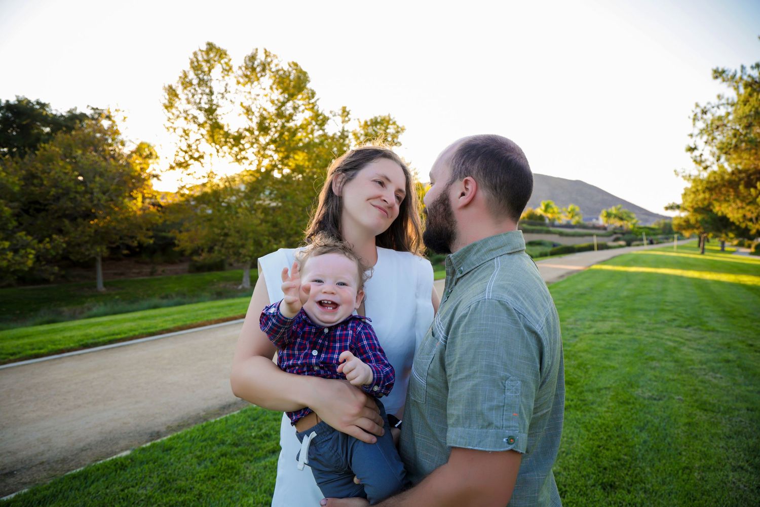 Family enjoys tender moments together in a sunlit park during golden hour sunset.