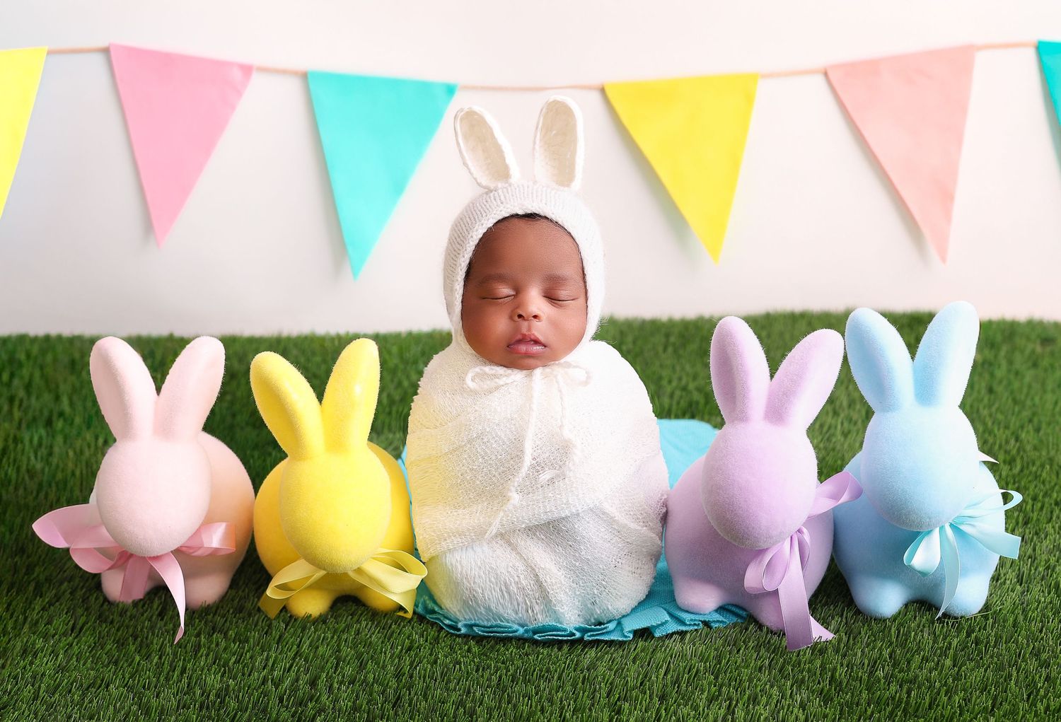 Colorful Easter bunny decorations and pastel bunting flags arranged on grass for spring holiday celebration.