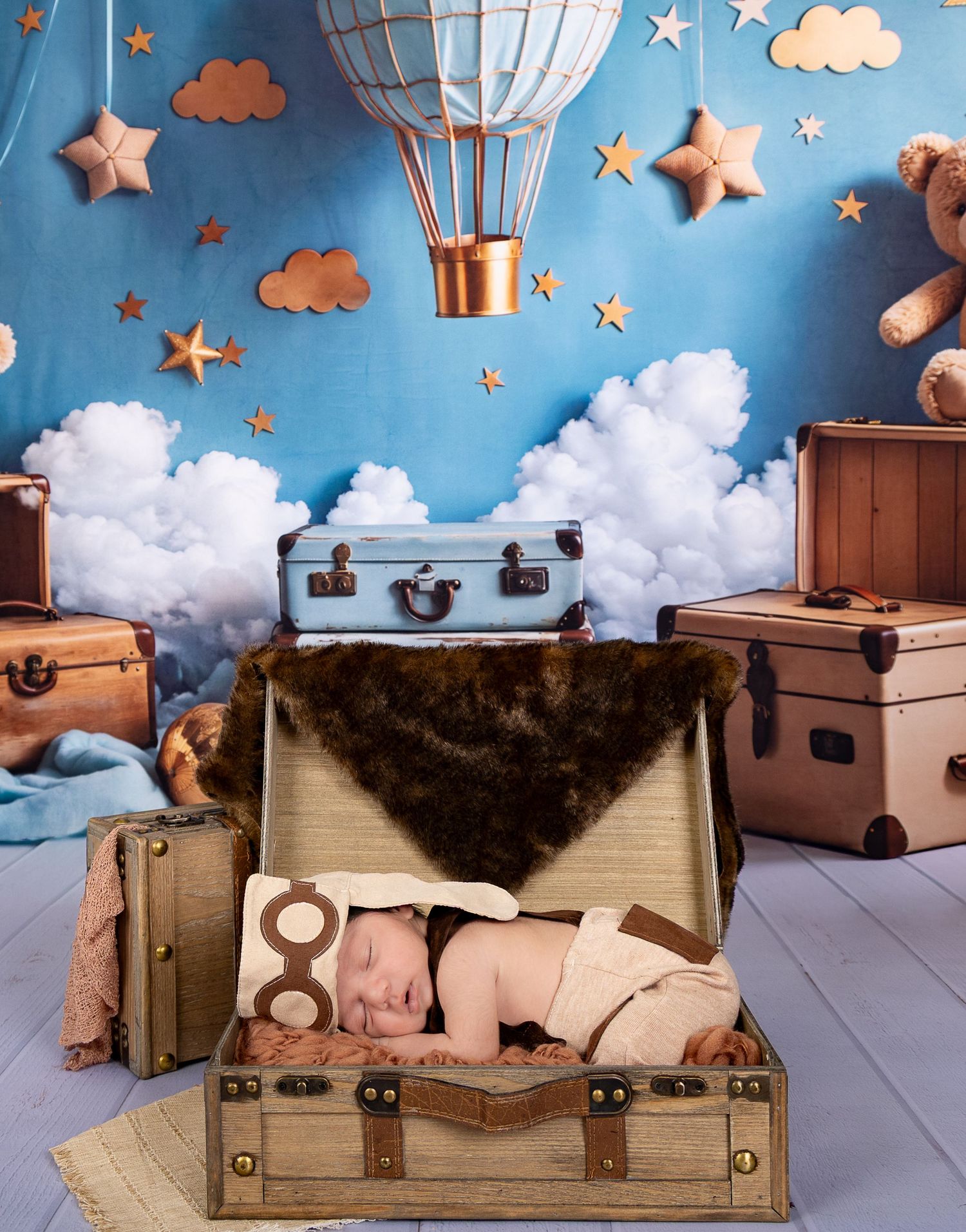 Whimsical nursery scene with vintage suitcases, hot air balloon, stars and clouds against blue backdrop.