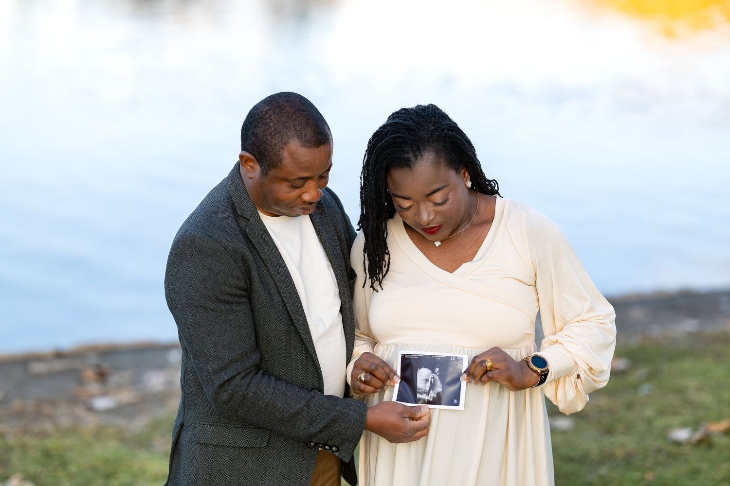 A couple stands outdoors looking at an ultrasound photo together with joyful expressions.