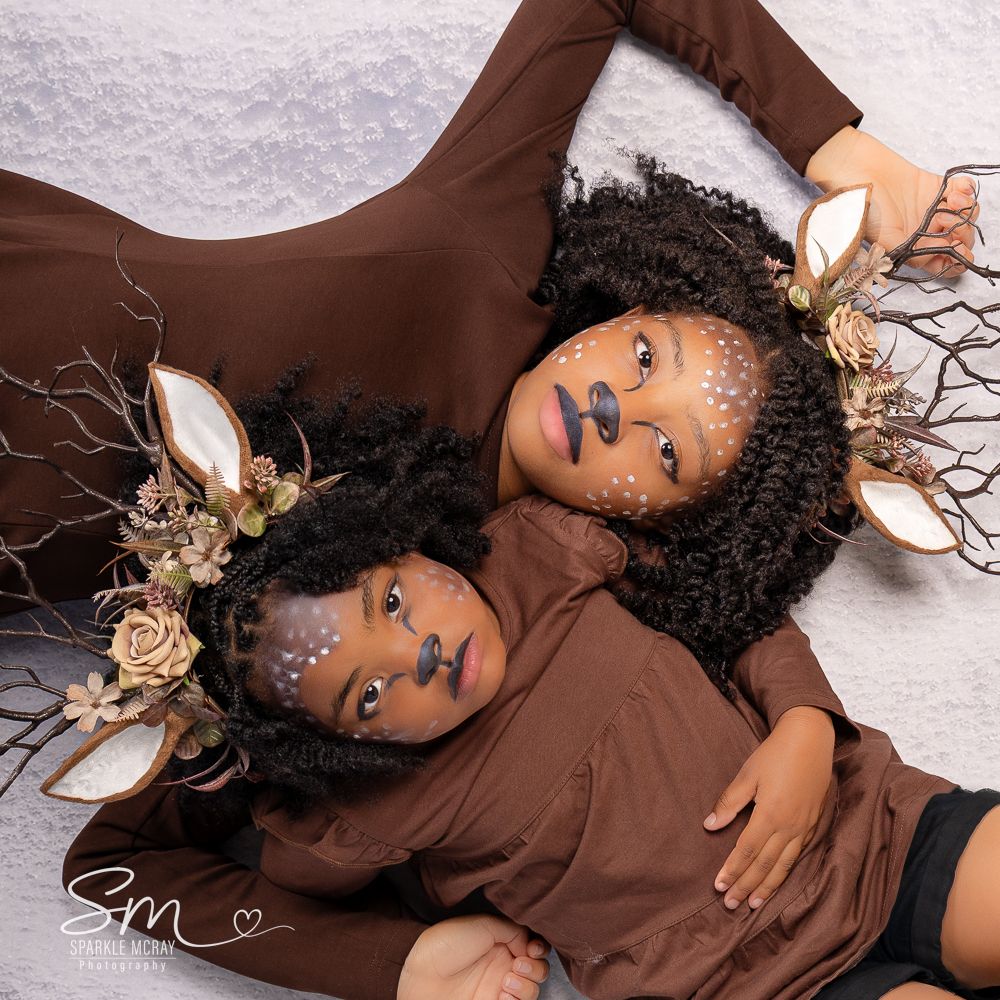 A person wearing a brown outfit lies on a white backdrop with gold floral accessories in a creative fashion photoshoot.