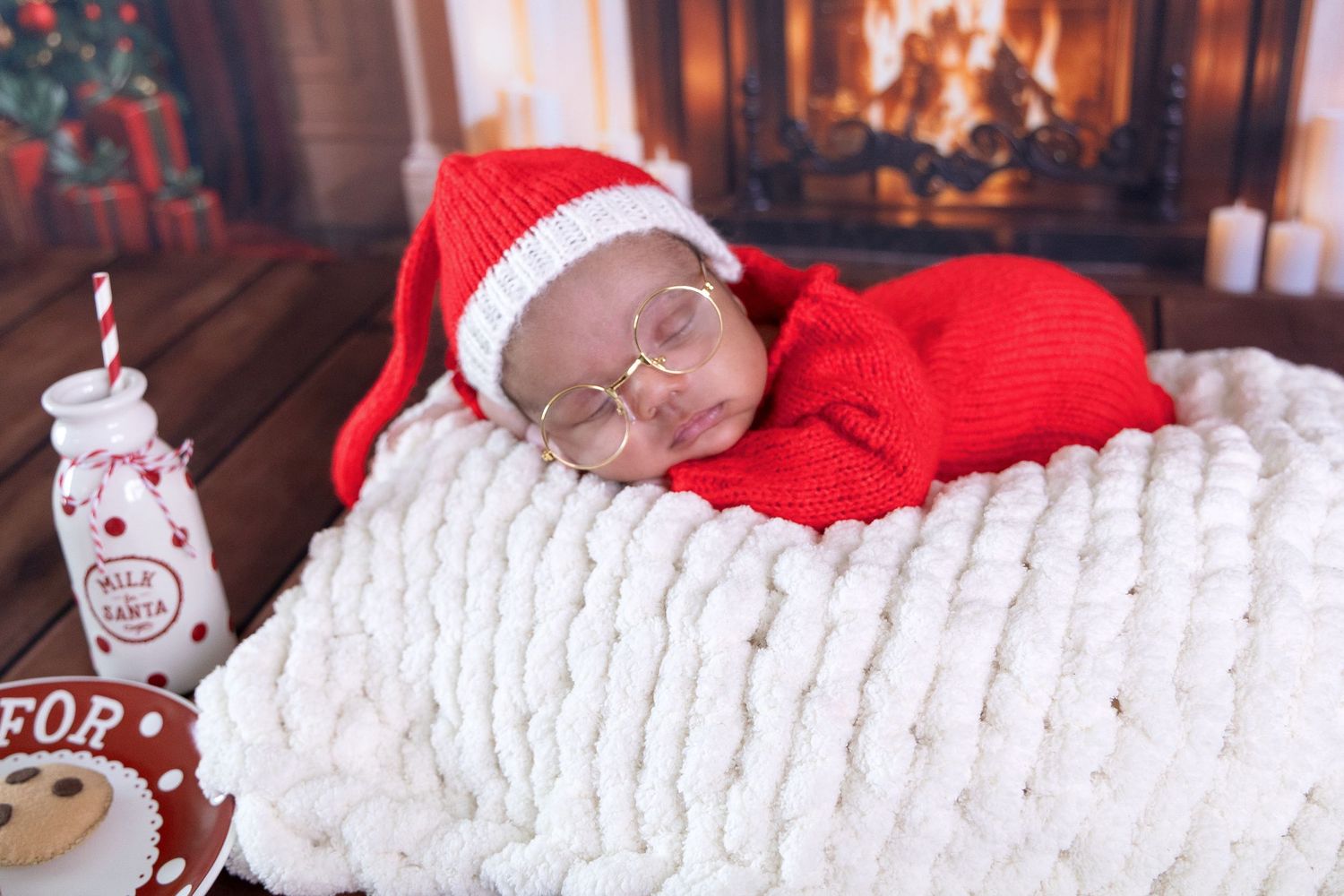 Newborn sleeping peacefully on white textured blanket with Christmas themed red outfit and decor.