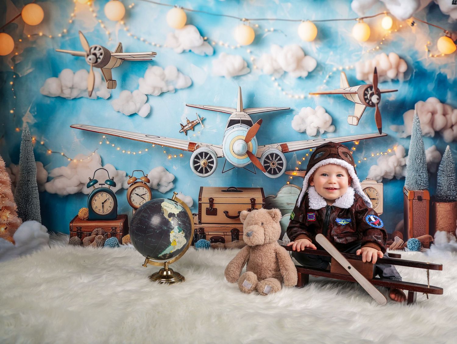 Vintage aviation themed setup with toy airplanes, teddy bear, and string lights against cloudy blue backdrop.