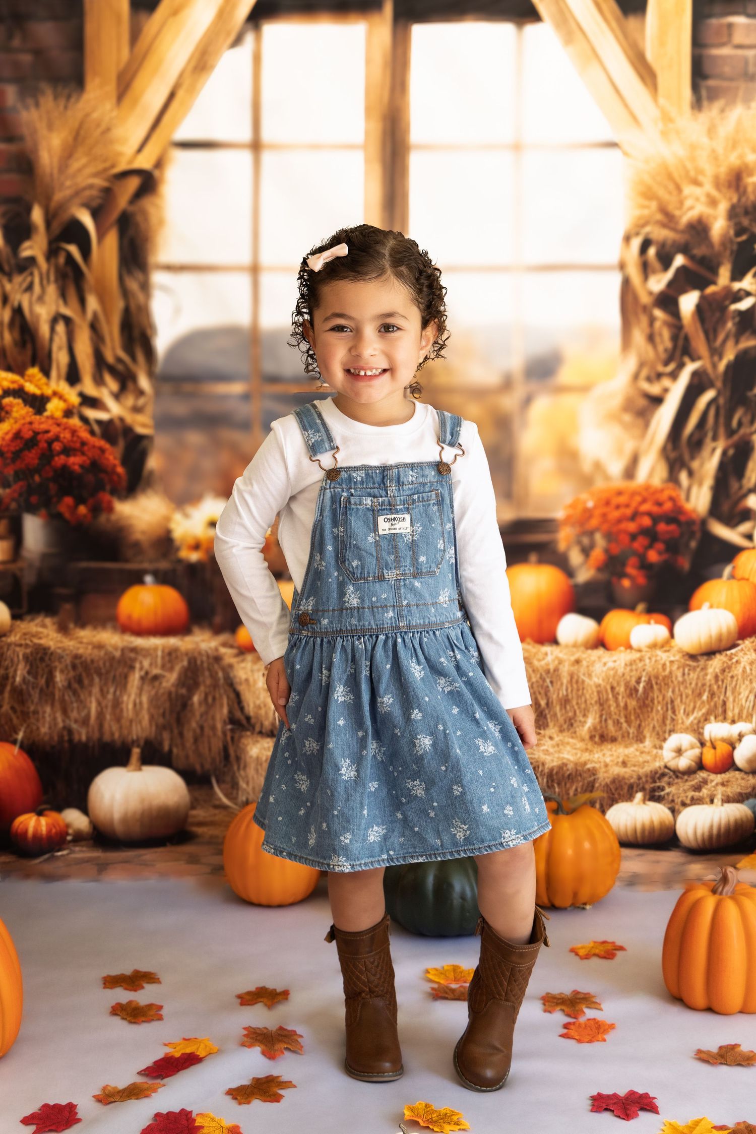Autumn scene with pumpkins, cornstalks, and fall decor featuring denim overalls and brown boots in rustic setting.