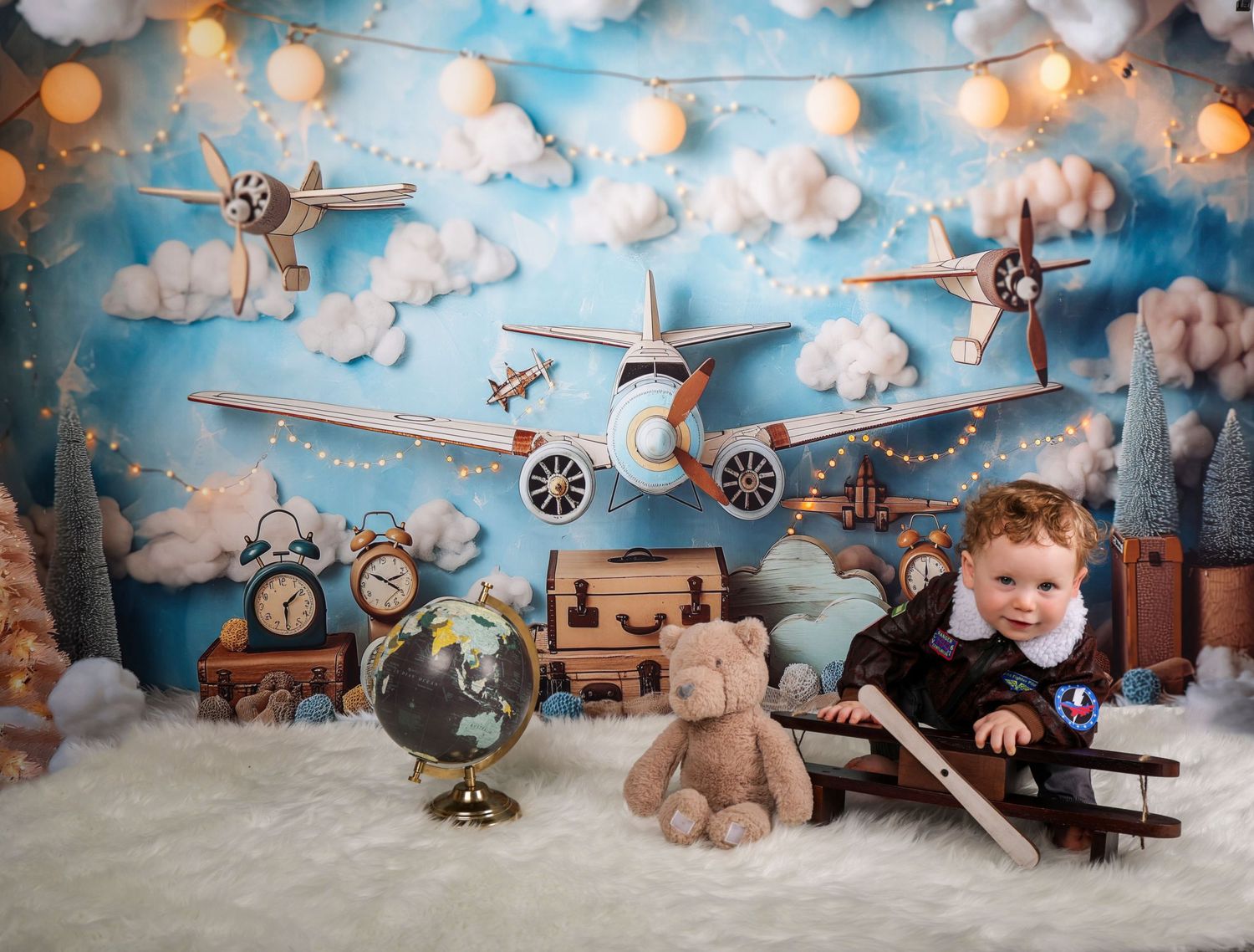 Vintage aviation themed setup with toy airplanes, teddy bear, and string lights against cloudy blue backdrop.