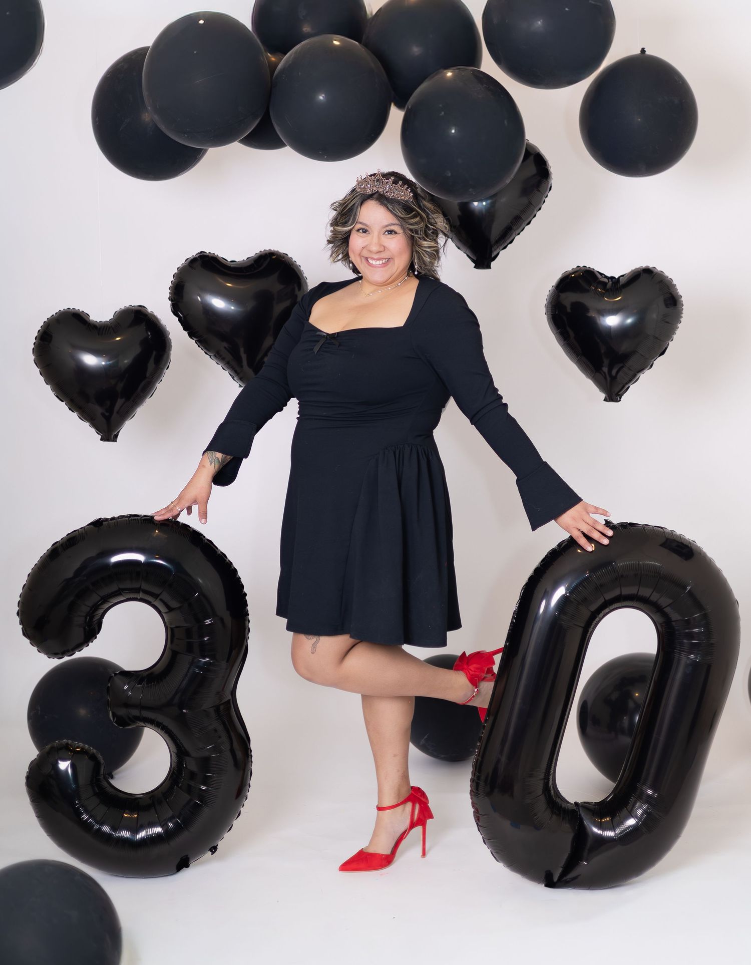 A collage of black balloons and number decorations in a modern monochromatic photoshoot setup with red accent heels.