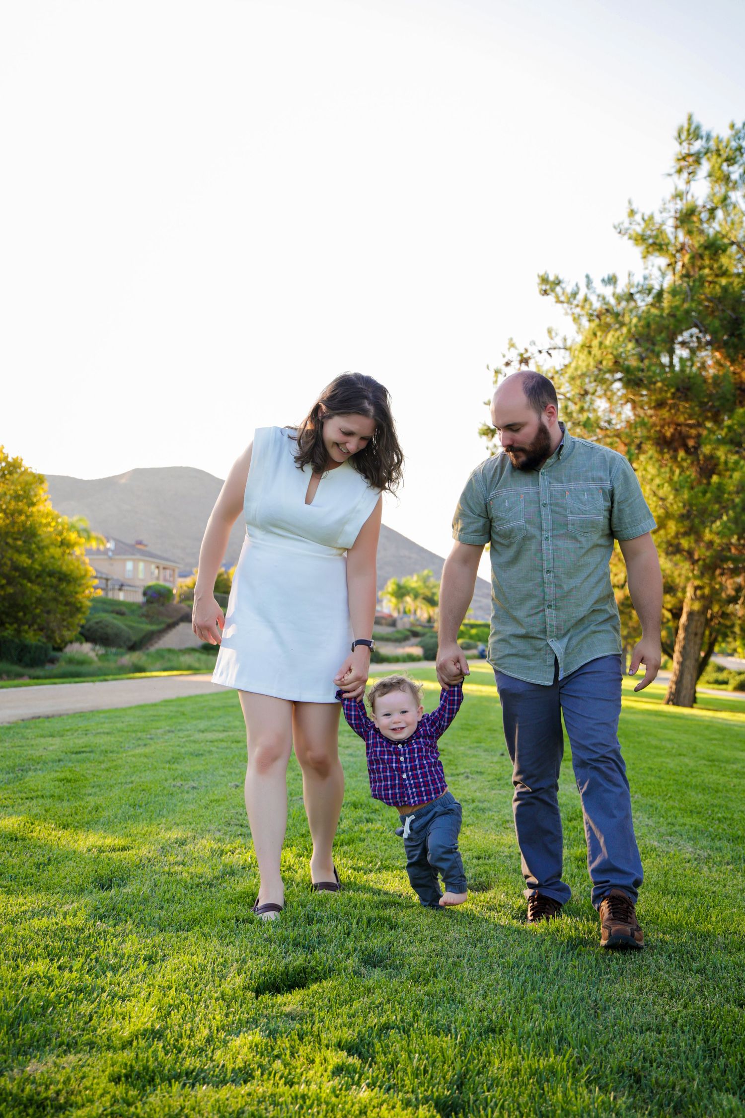 A family walks together on a grassy hillside during golden hour as sunlight illuminates the landscape.