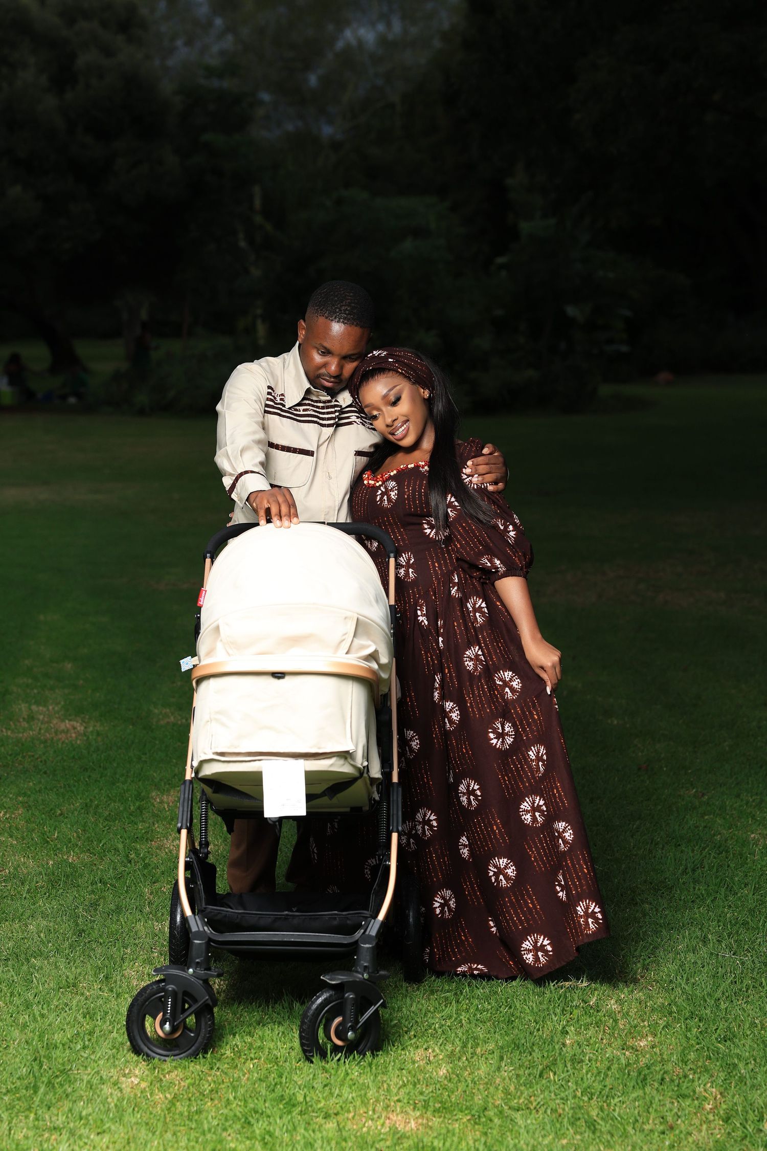 Happy African American couple with baby stroller enjoying a sunny day in a lush green park.