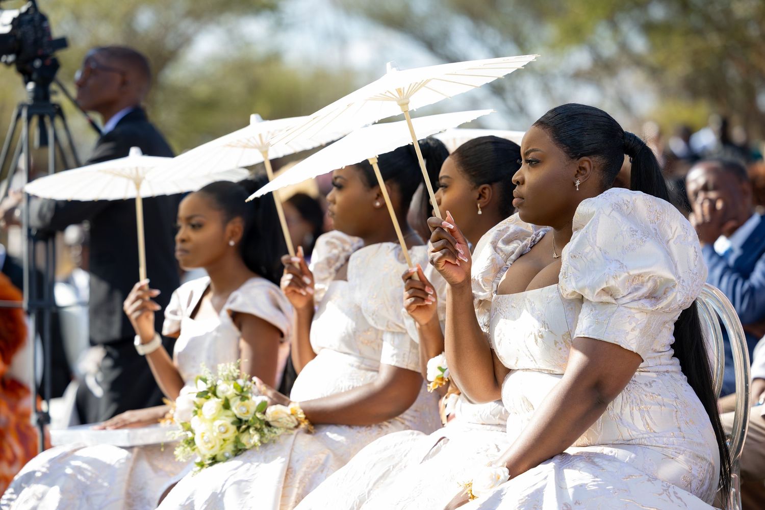Wedding party members holding white parasols during outdoor celebration.