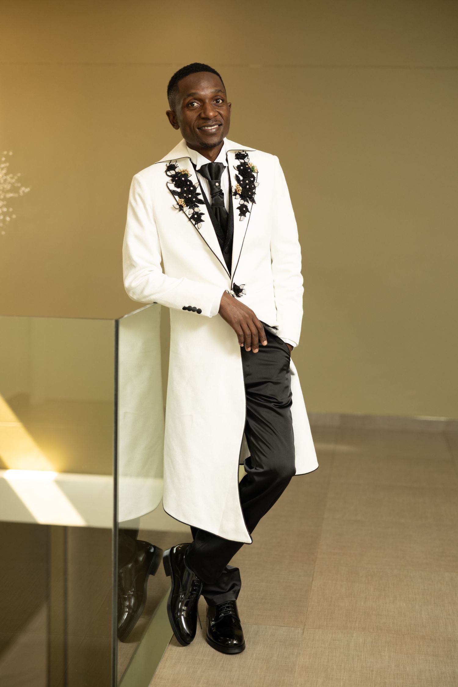 Person in white tuxedo jacket and black pants poses against golden-lit background.