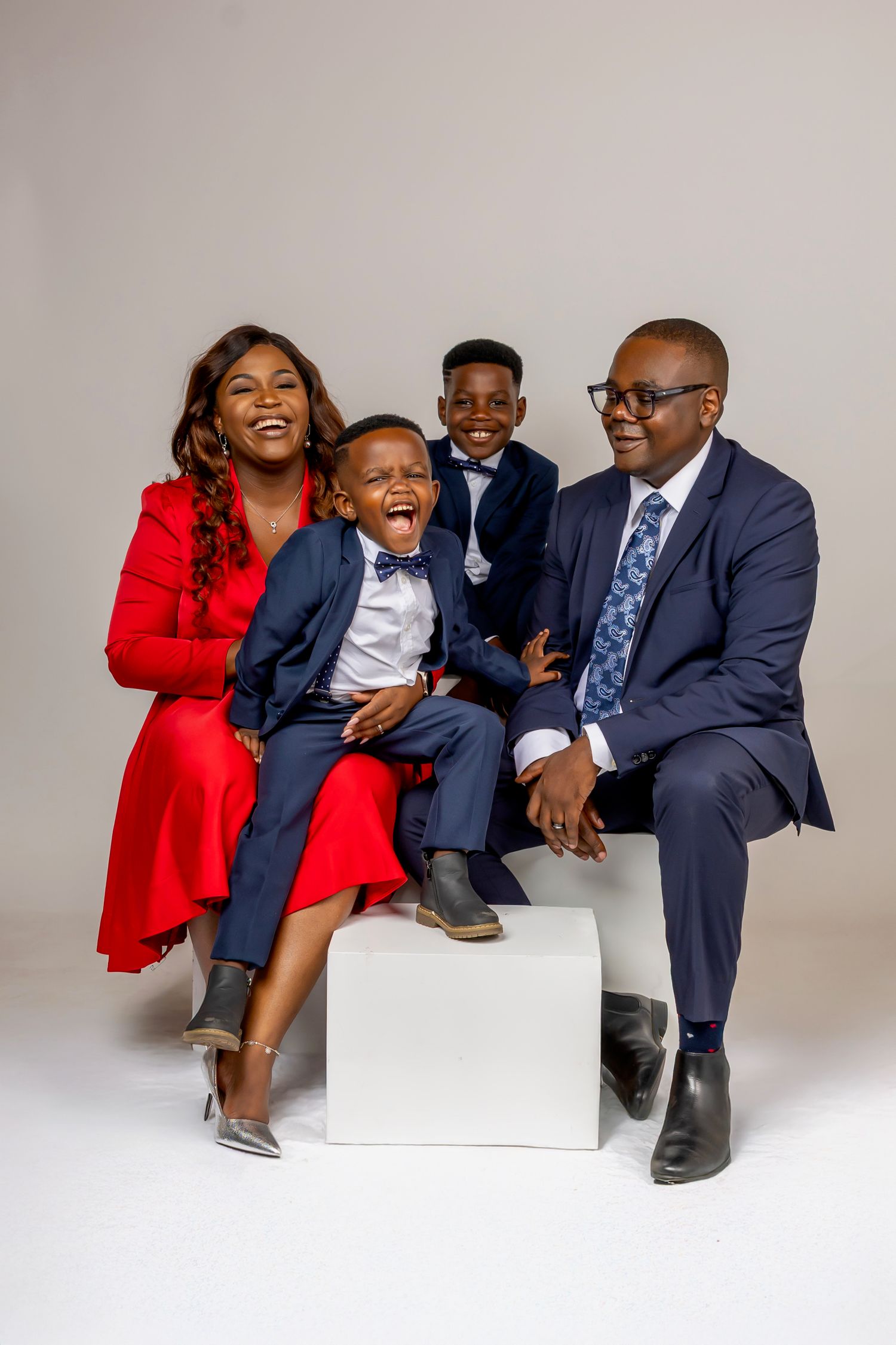 A family portrait session with coordinated navy and red outfits sitting on white blocks against a neutral backdrop.