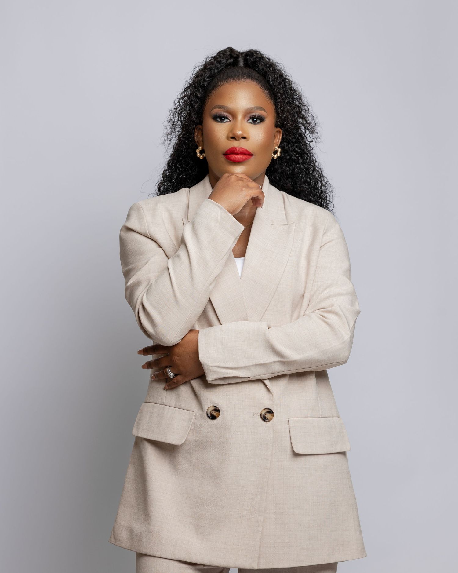 Professional studio portrait of someone wearing a cream-colored double-breasted blazer against a gray background.