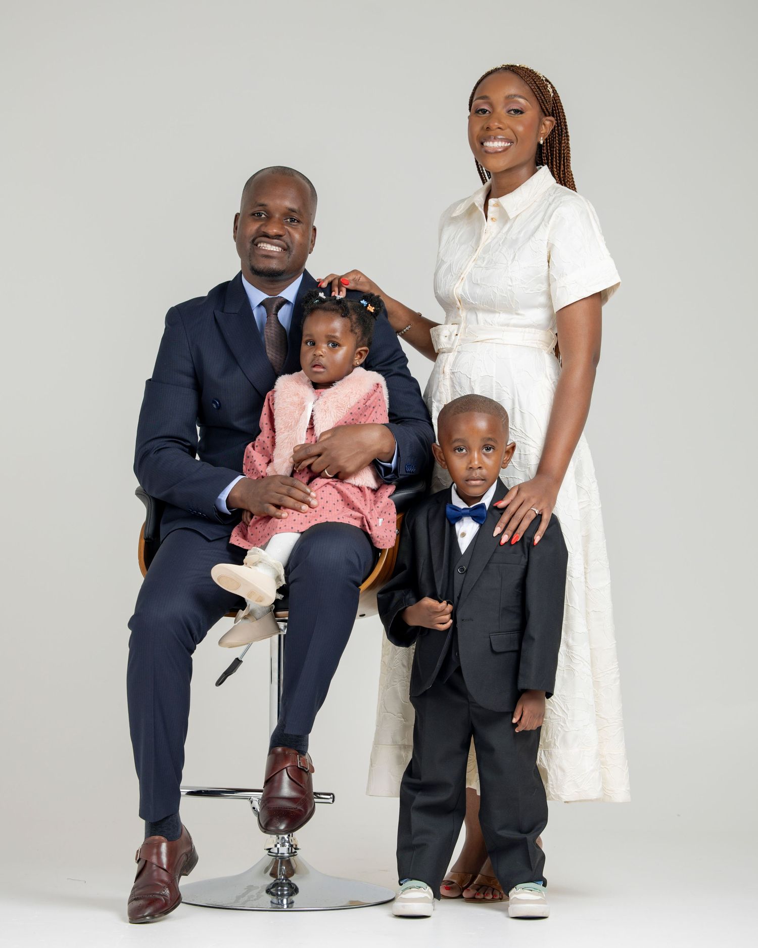 Family portrait of parents and two young children dressed in formal attire posing in a studio setting.