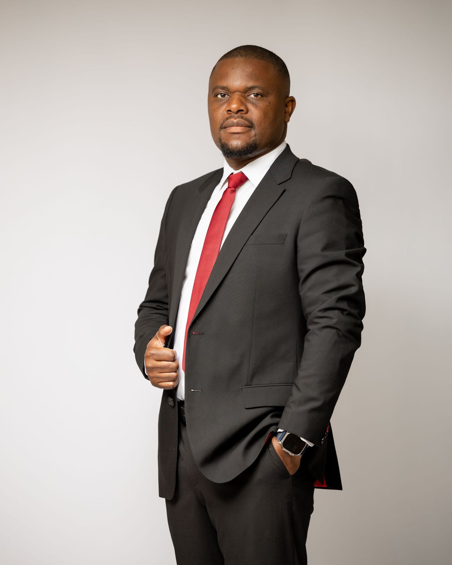 Professional in dark suit and red tie poses against white background.