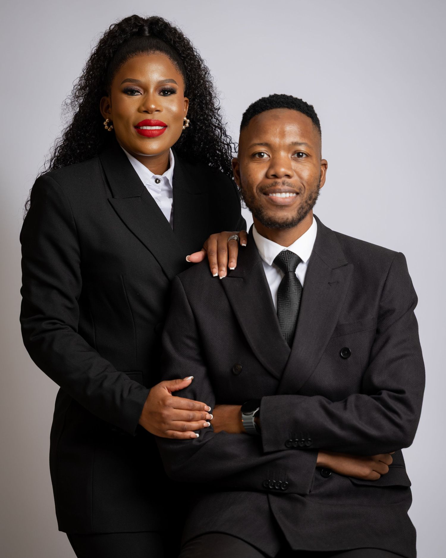 Professional studio portraits of a couple in matching black formal attire posing together against a light gray background.