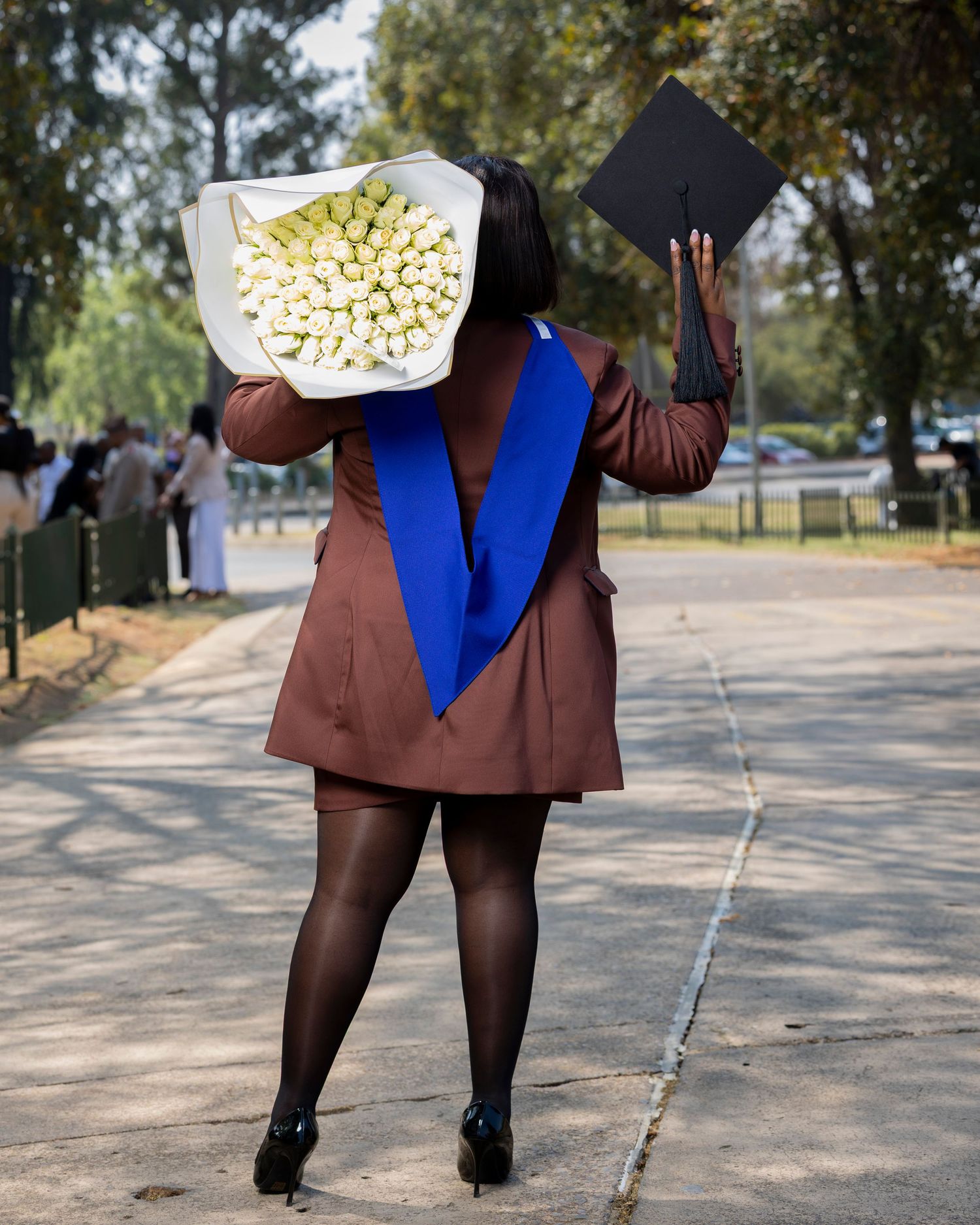 Series of lower body shots showing person in blue dress and brown jacket walking outdoors.