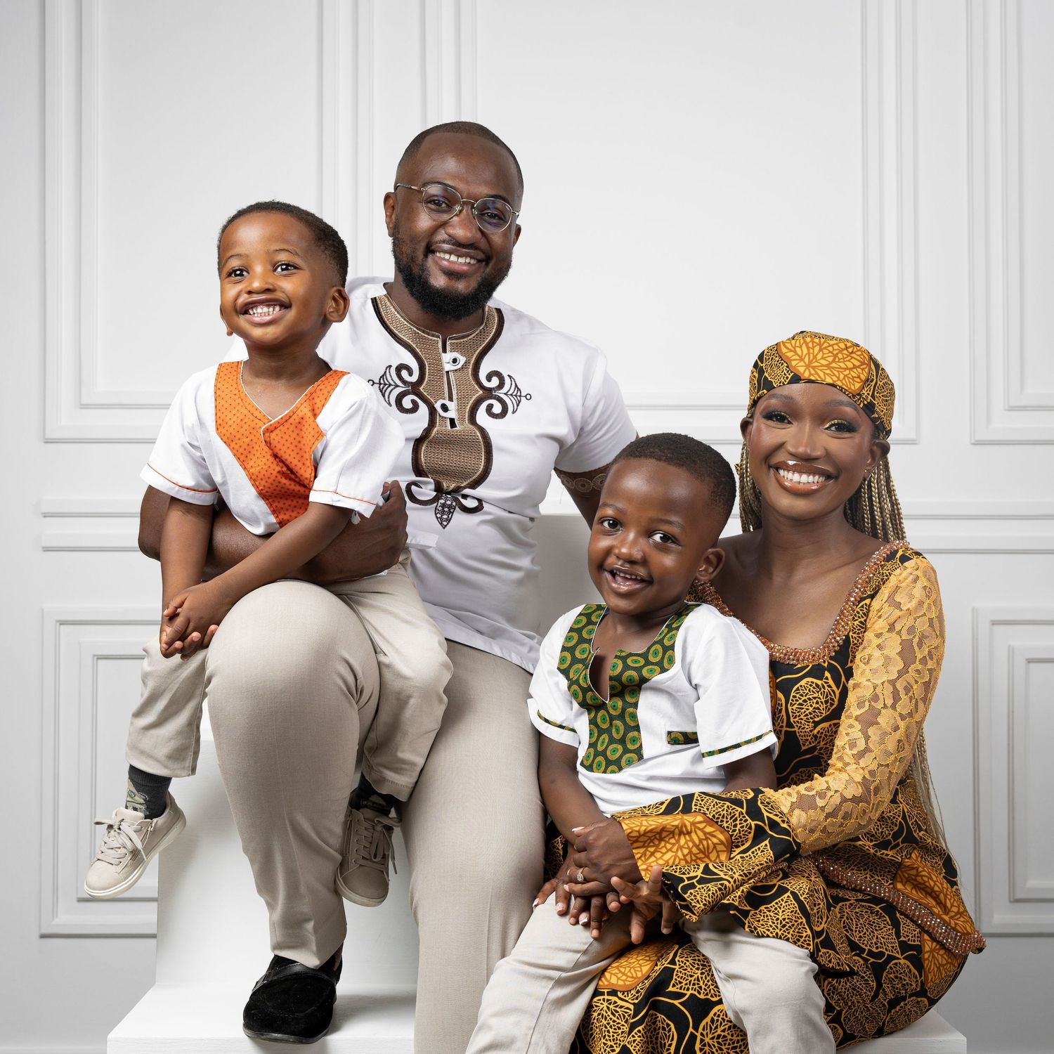 A joyful African family of four in matching traditional attire posing for a portrait against a white background.