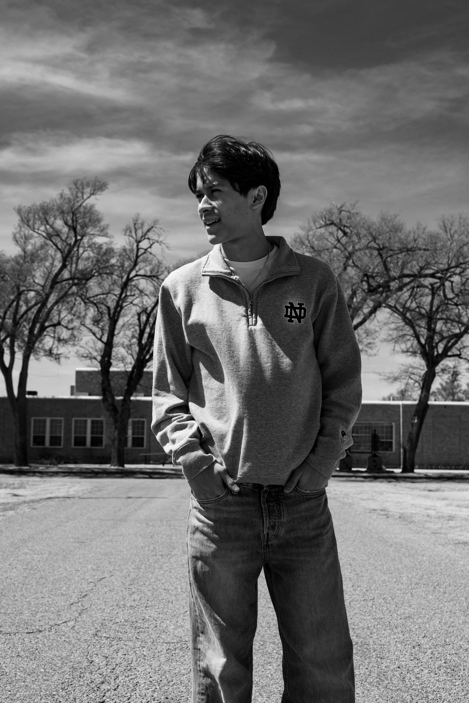 Black and white portrait of a young man wearing a Notre Dame quarter-zip sweater in a school parking lot.