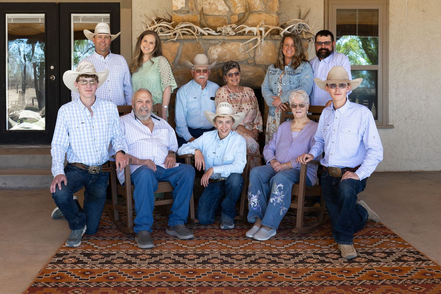 Large family group portrait of eleven people in western attire posed on a rustic porch with decorative antlers.