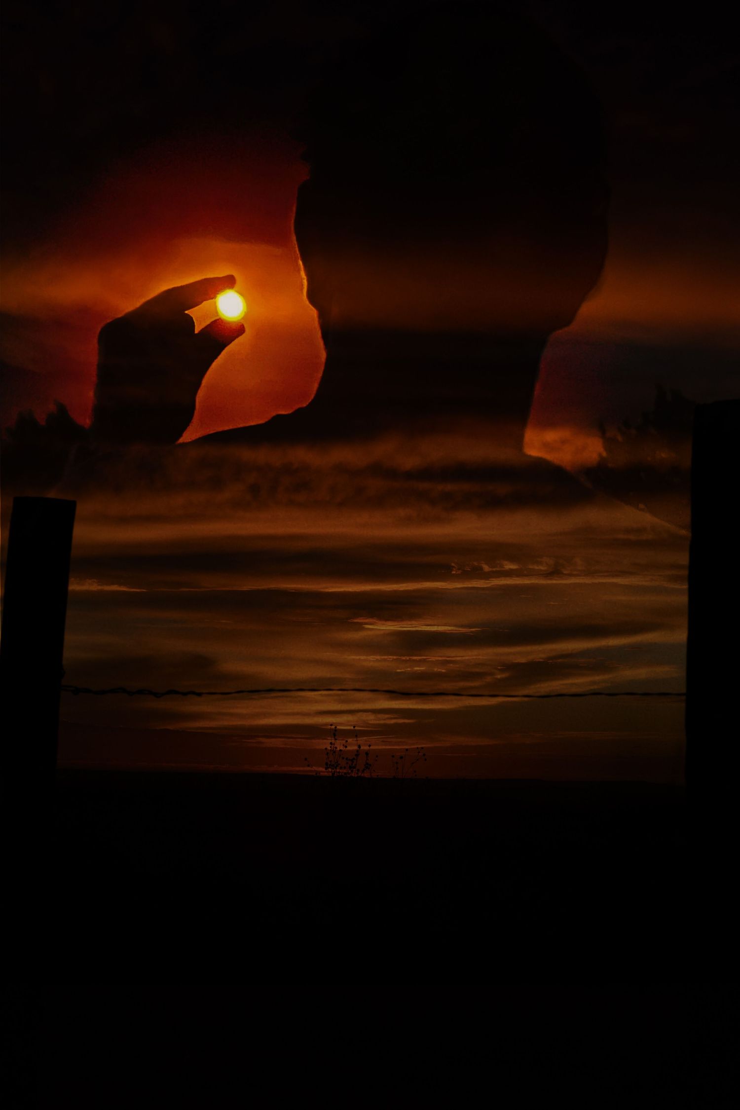 Silhouette of a person holding the glowing sun against a dramatic orange sunset sky.