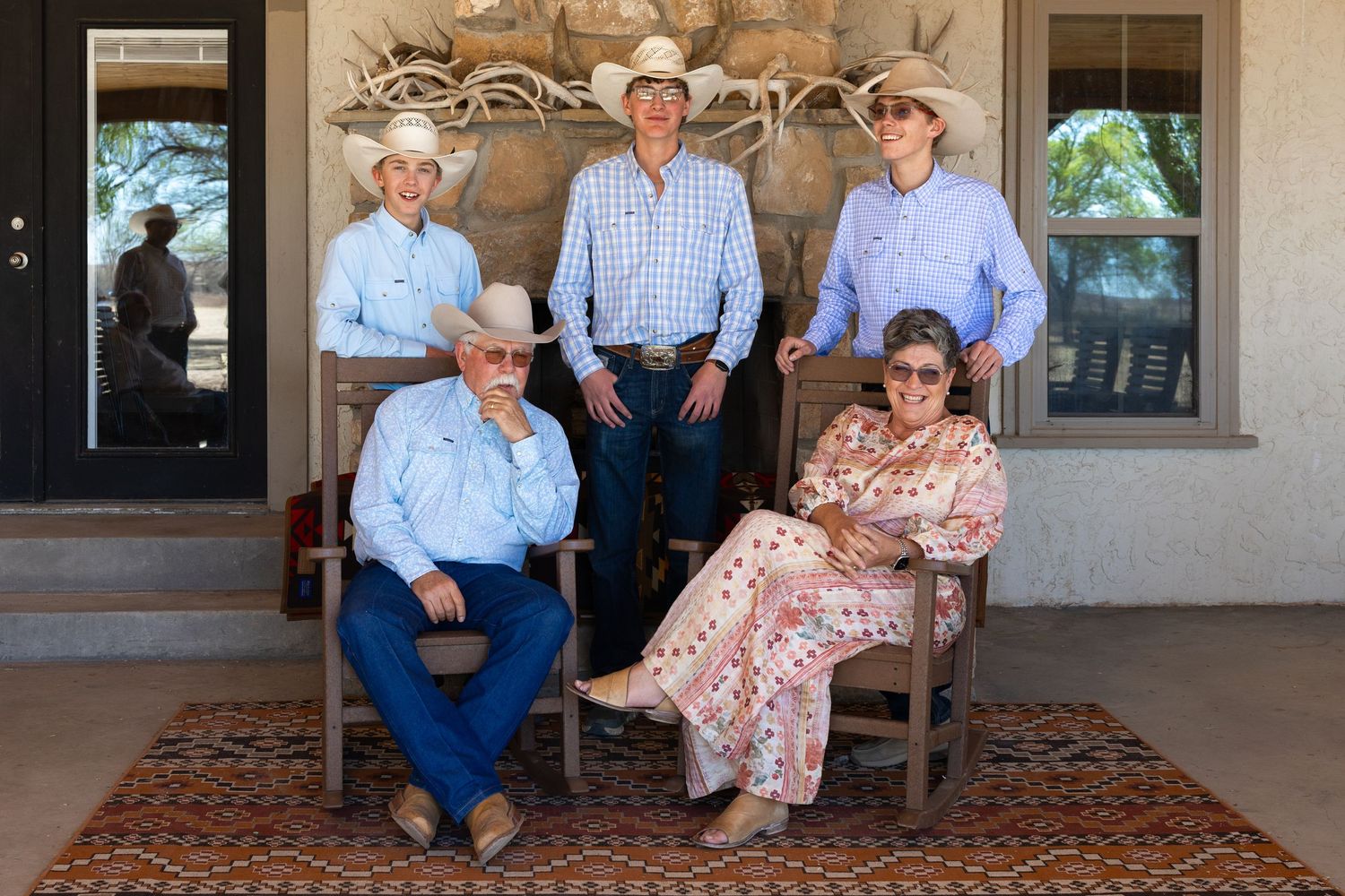 Five family members in cowboy hats and western wear pose on a ranch porch with antler wall decor.