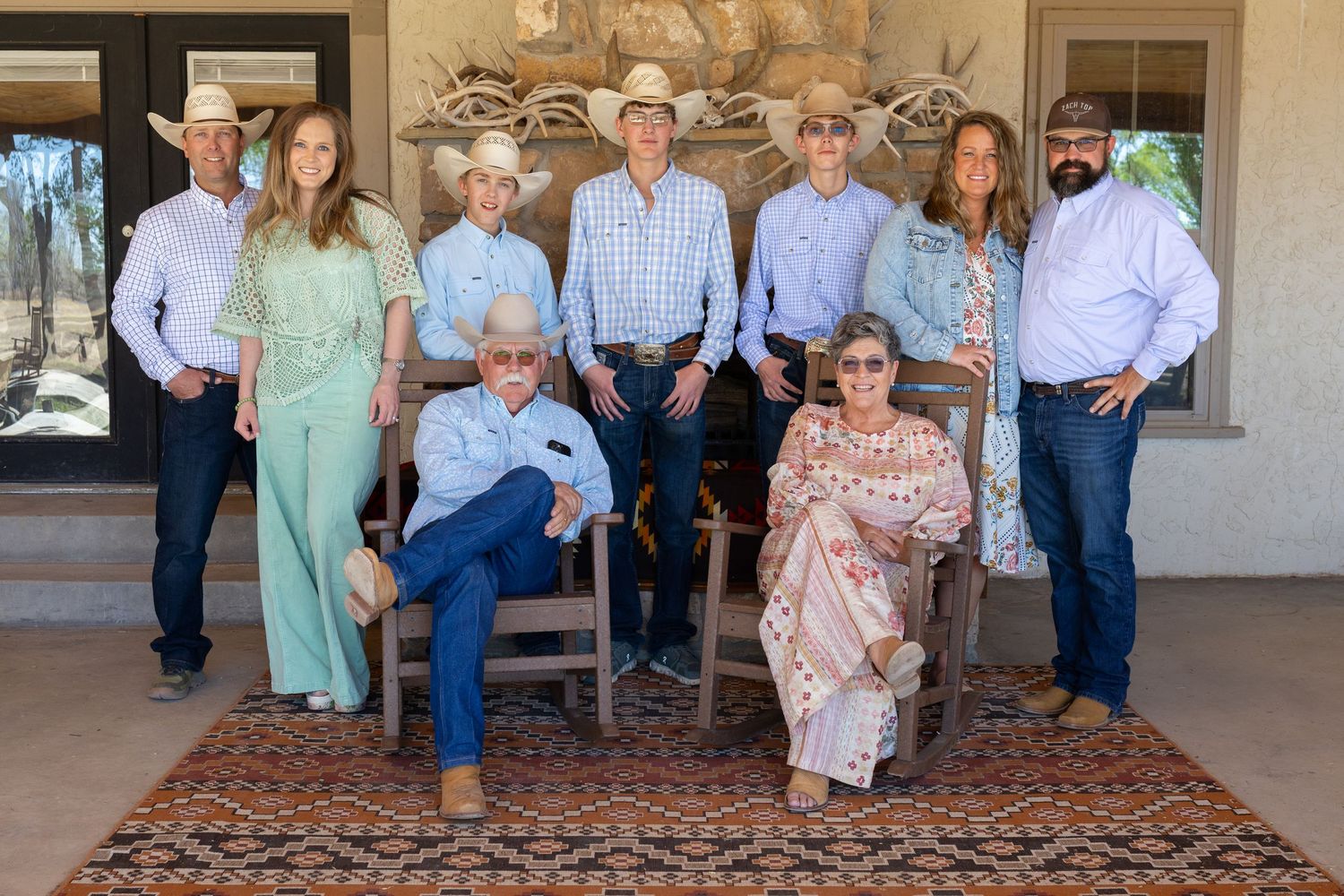 Nine family members in western attire pose on a ranch porch with antler decor and southwestern rug.
