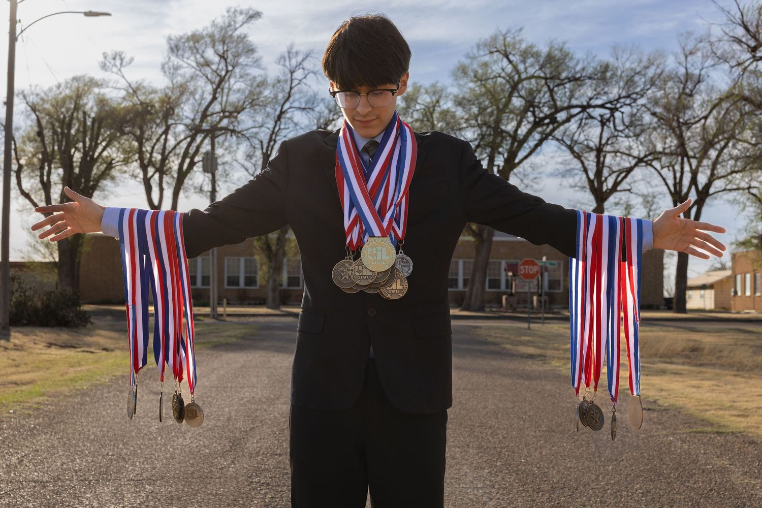 Young man in a suit proudly displaying numerous competition medals with red, white, and blue ribbons.