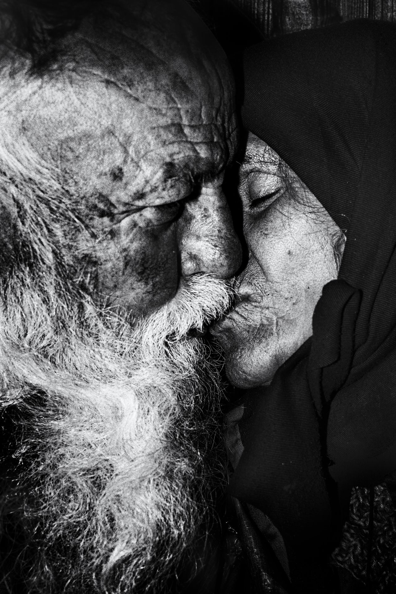 An intimate black and white portrait of an elderly couple sharing love and a tender kiss, captured on film by Roland Kilimanjaro.