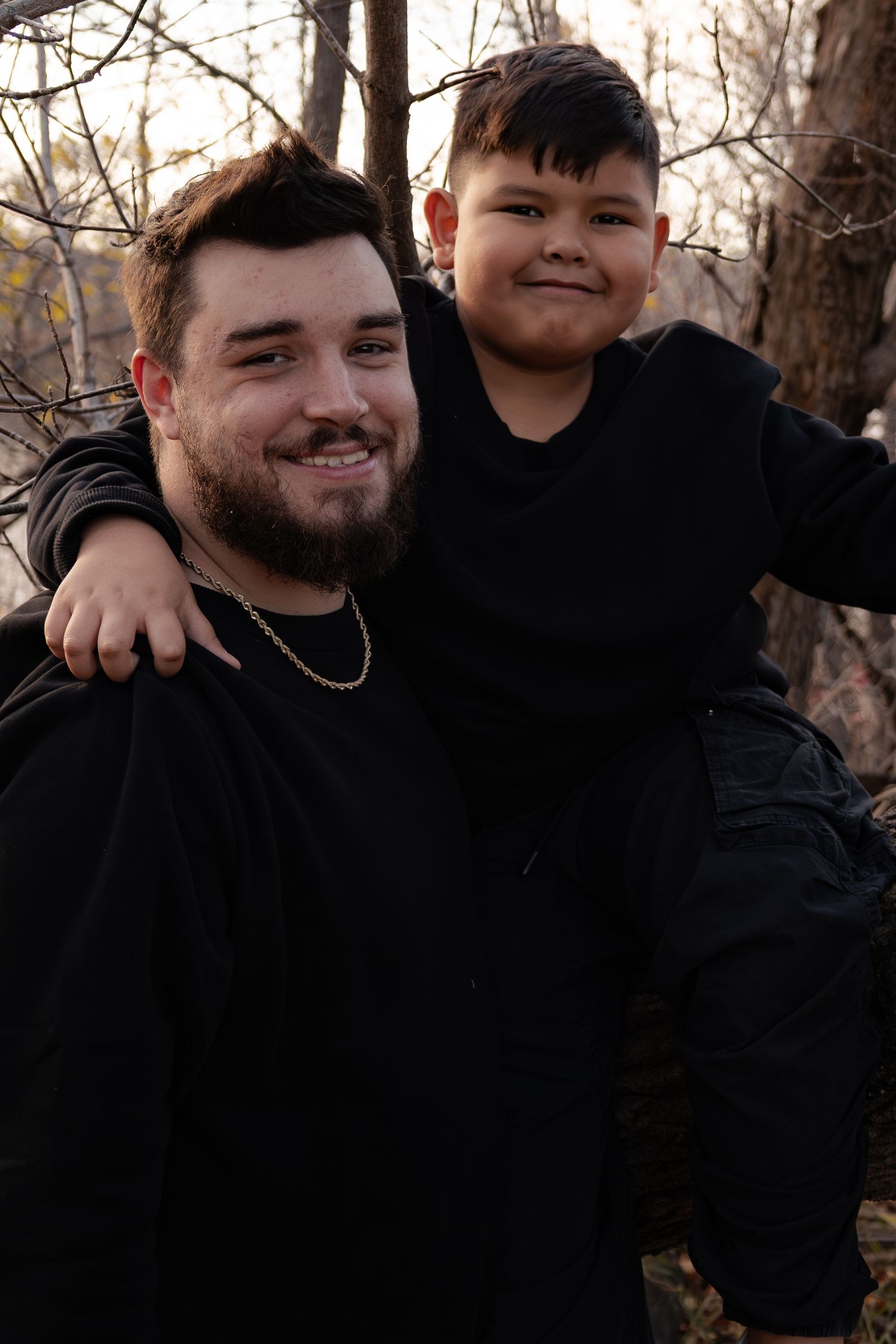 Smiling bearded man in black sweatshirt giving young boy a piggyback ride in autumn outdoor setting in Winnipeg