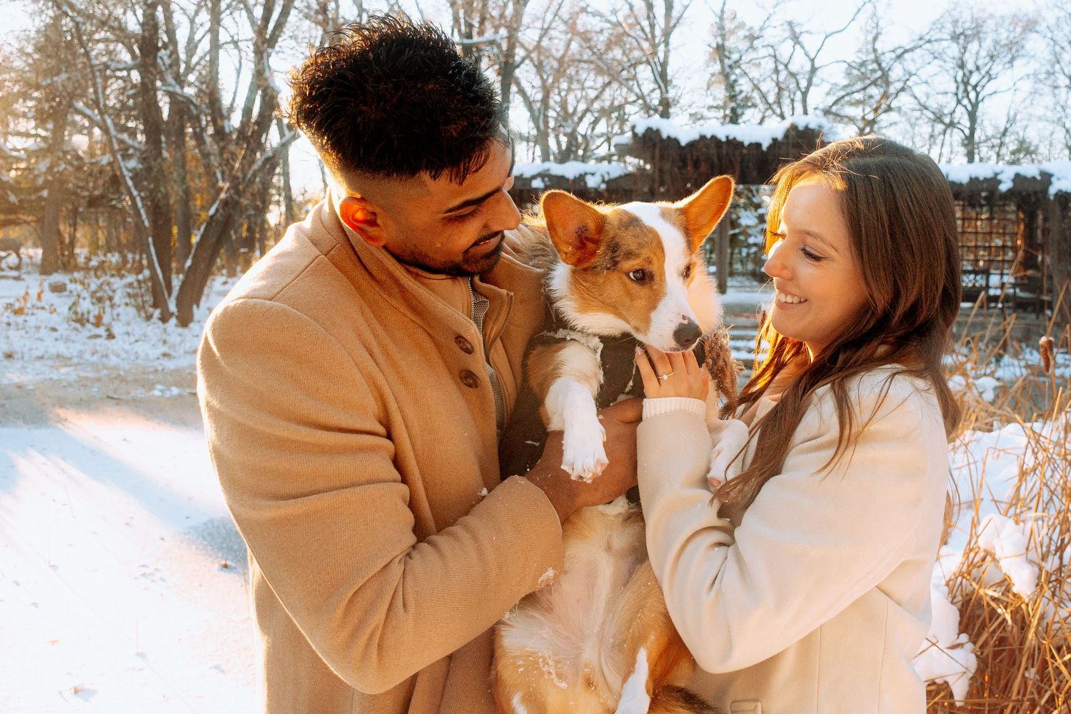 Happy couple holding an adorable corgi puppy outdoors in a snowy winter landscape in Winnipeg