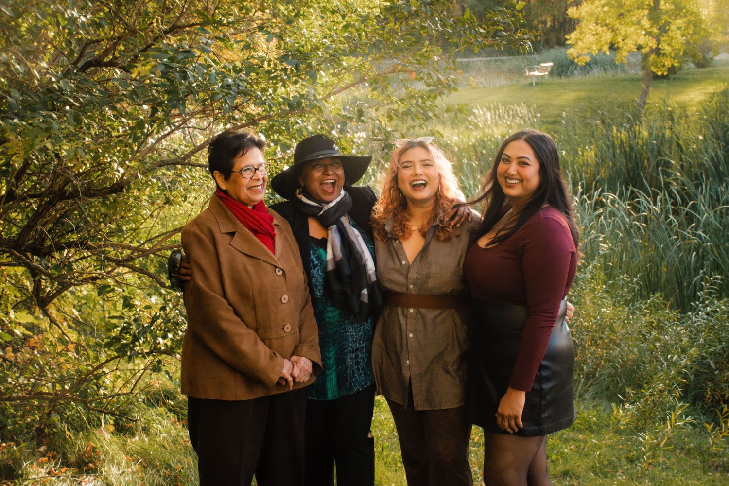 Four women smiling together outdoors in autumn foliage with golden sunlight behind them in Winnipeg