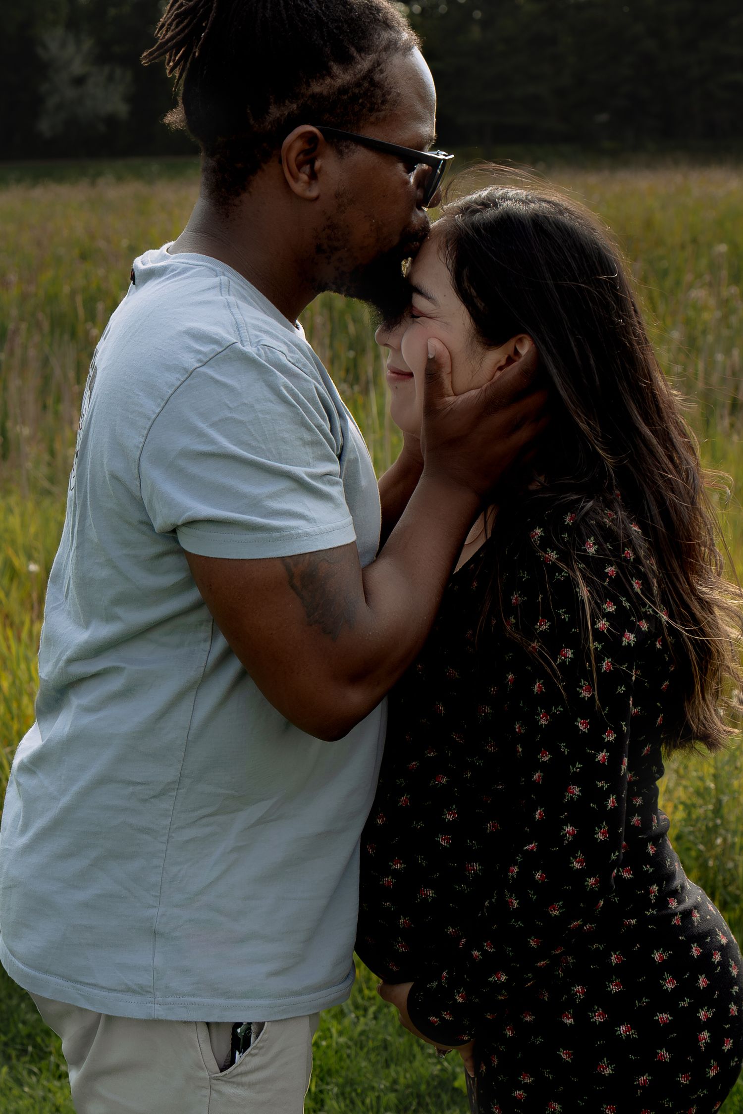 Couple sharing an intimate moment in a meadow, man gently cupping womans face as they lean in to kiss  in Winnipeg