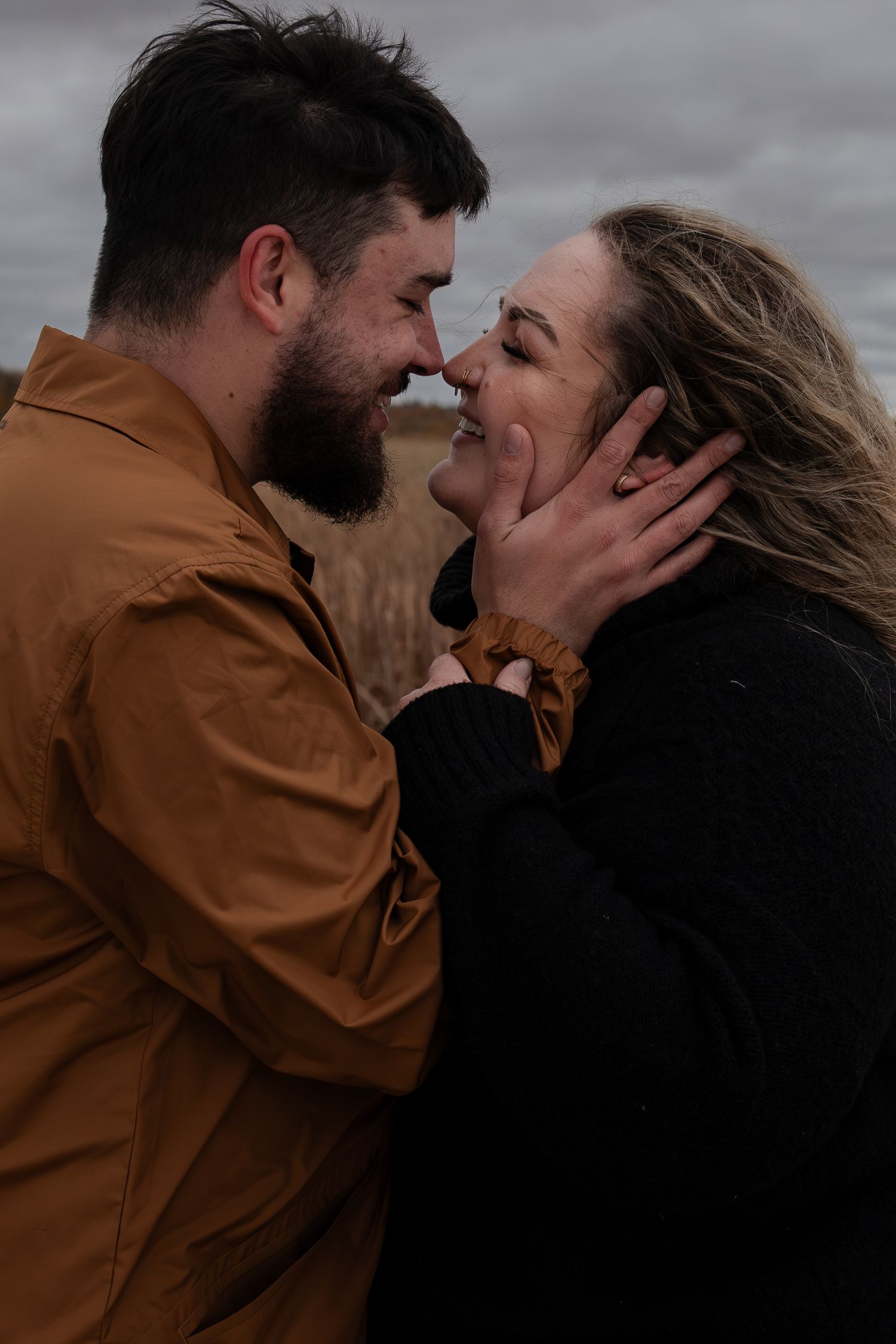 Bearded man in brown jacket and woman in black sweater sharing a tender nose-to-nose moment outdoors in Winnipeg