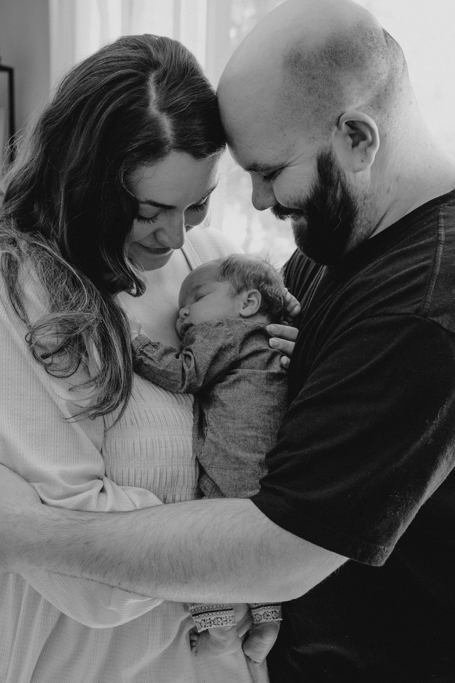 Black and white photo of new parents tenderly holding their newborn baby, foreheads touching in a loving embrace.