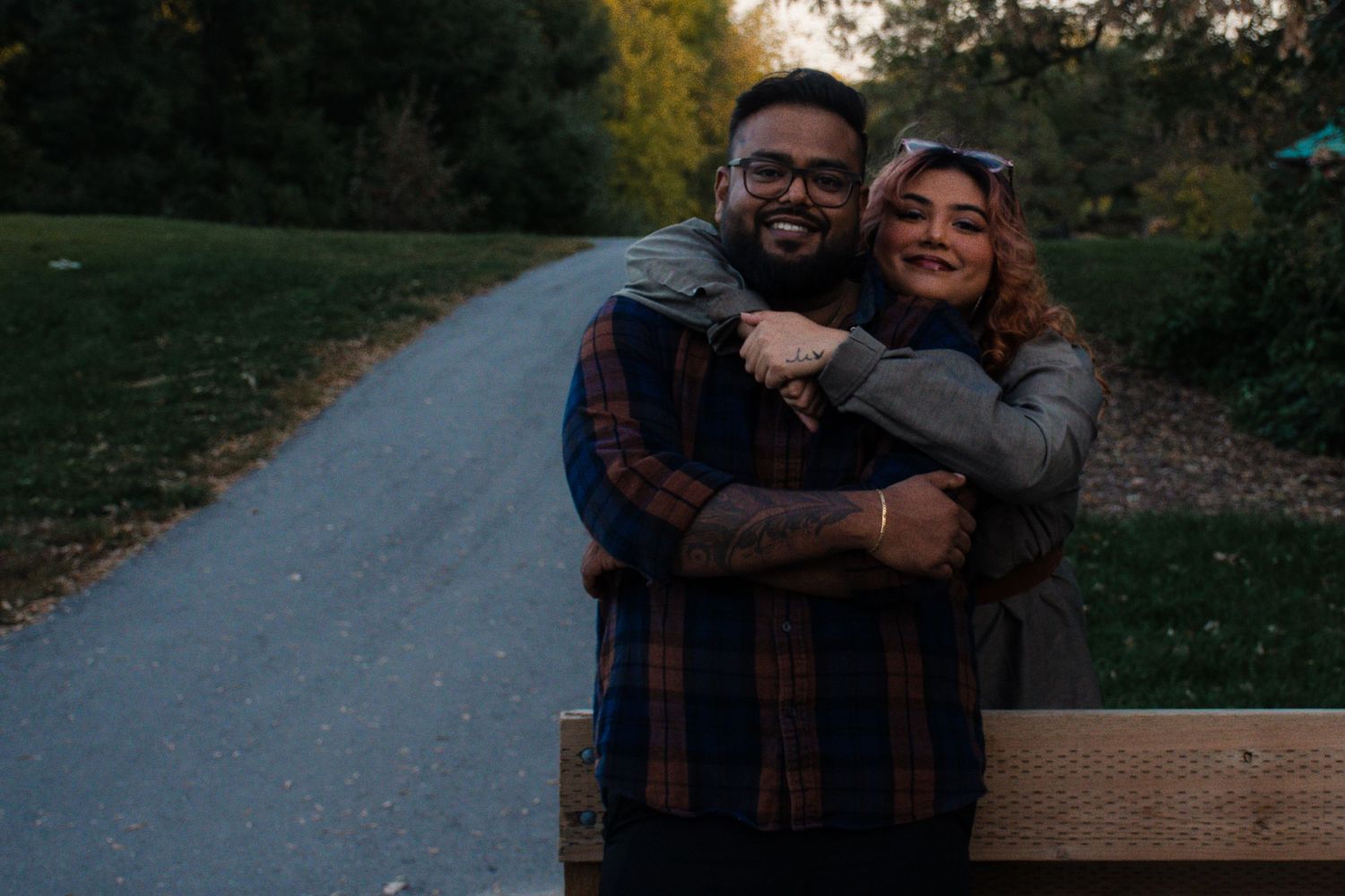 A brother and sister embrace and smile on a park path surrounded by autumn foliage in Winnipeg